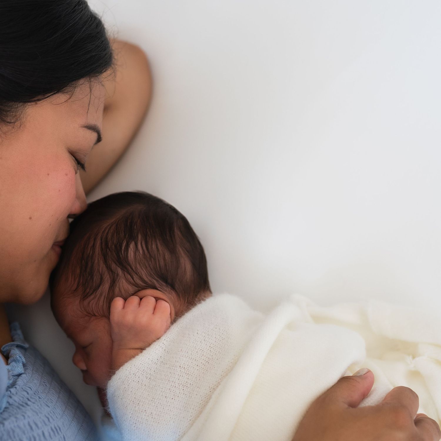 Intimate newborn moment captured with soft white blanket against white background.