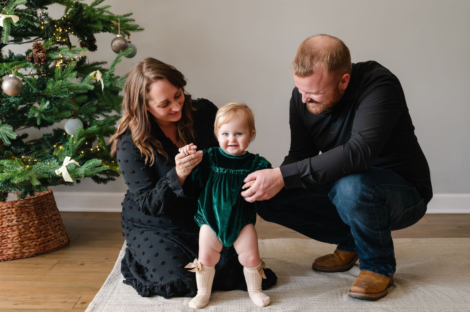 Family plays and laughs together in front of decorated Christmas tree during holiday photoshoot.