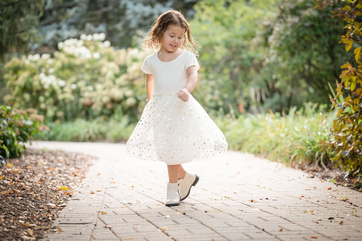 A young girl in a white dress twirls on a garden path.