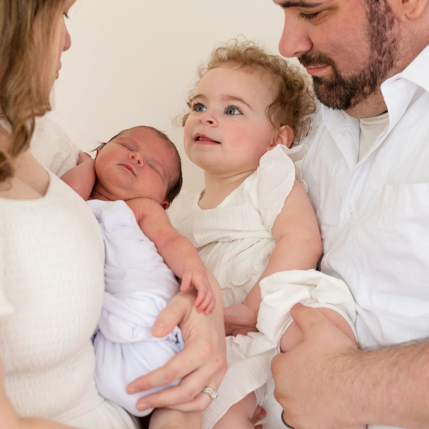 A family welcomes their newborn baby while an older sibling looks on with curiosity.