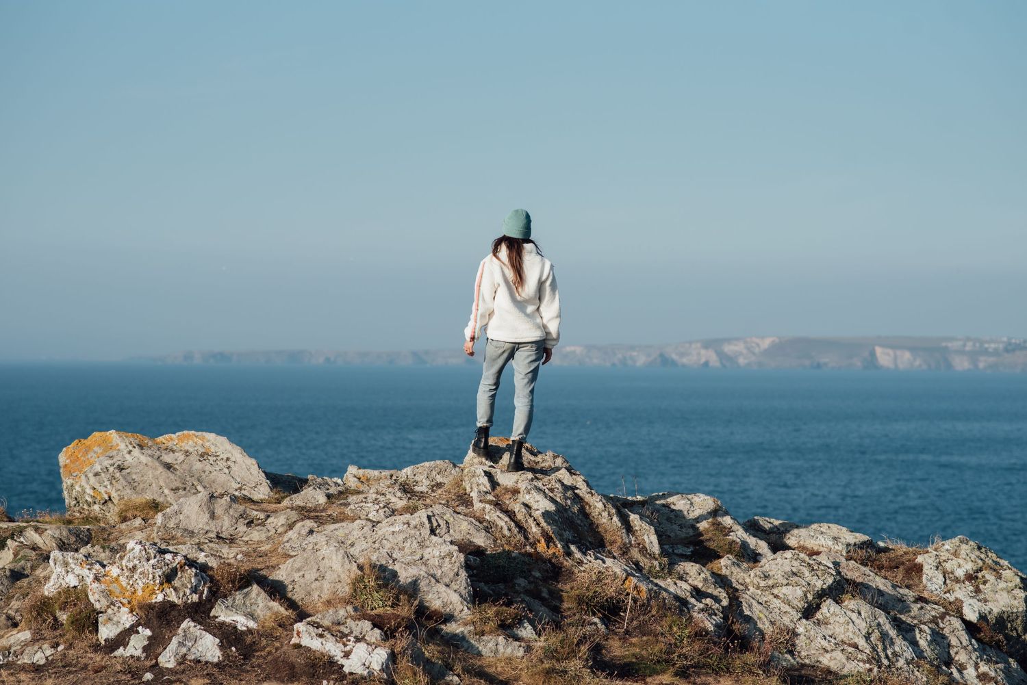Silhouette of person standing on coastal rocks overlooking ocean cliffs.