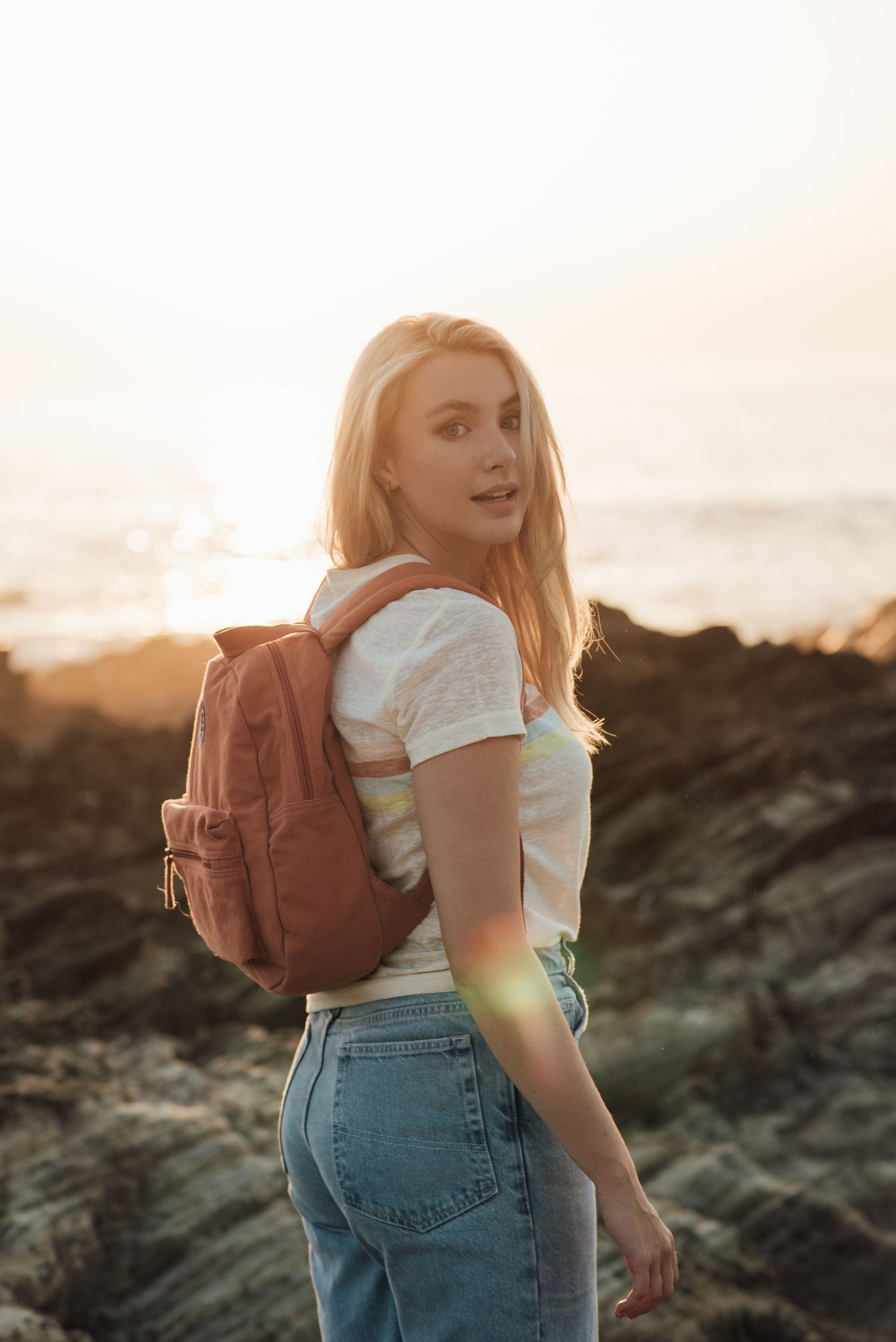 Adventure seeker with backpack exploring rocky coastline at golden hour.