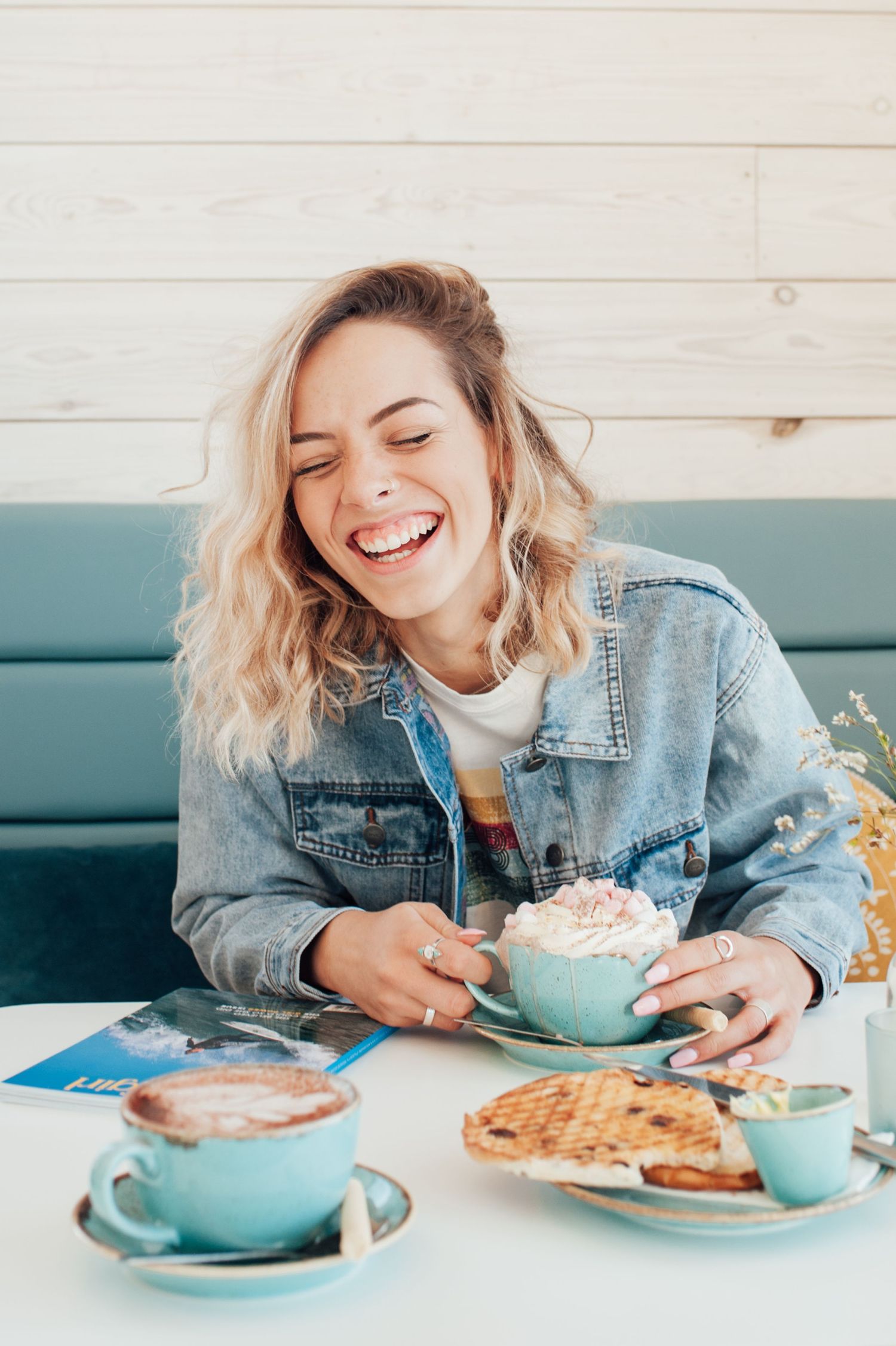 Person enjoying breakfast with waffles and whipped cream at a cafe with blue cups.