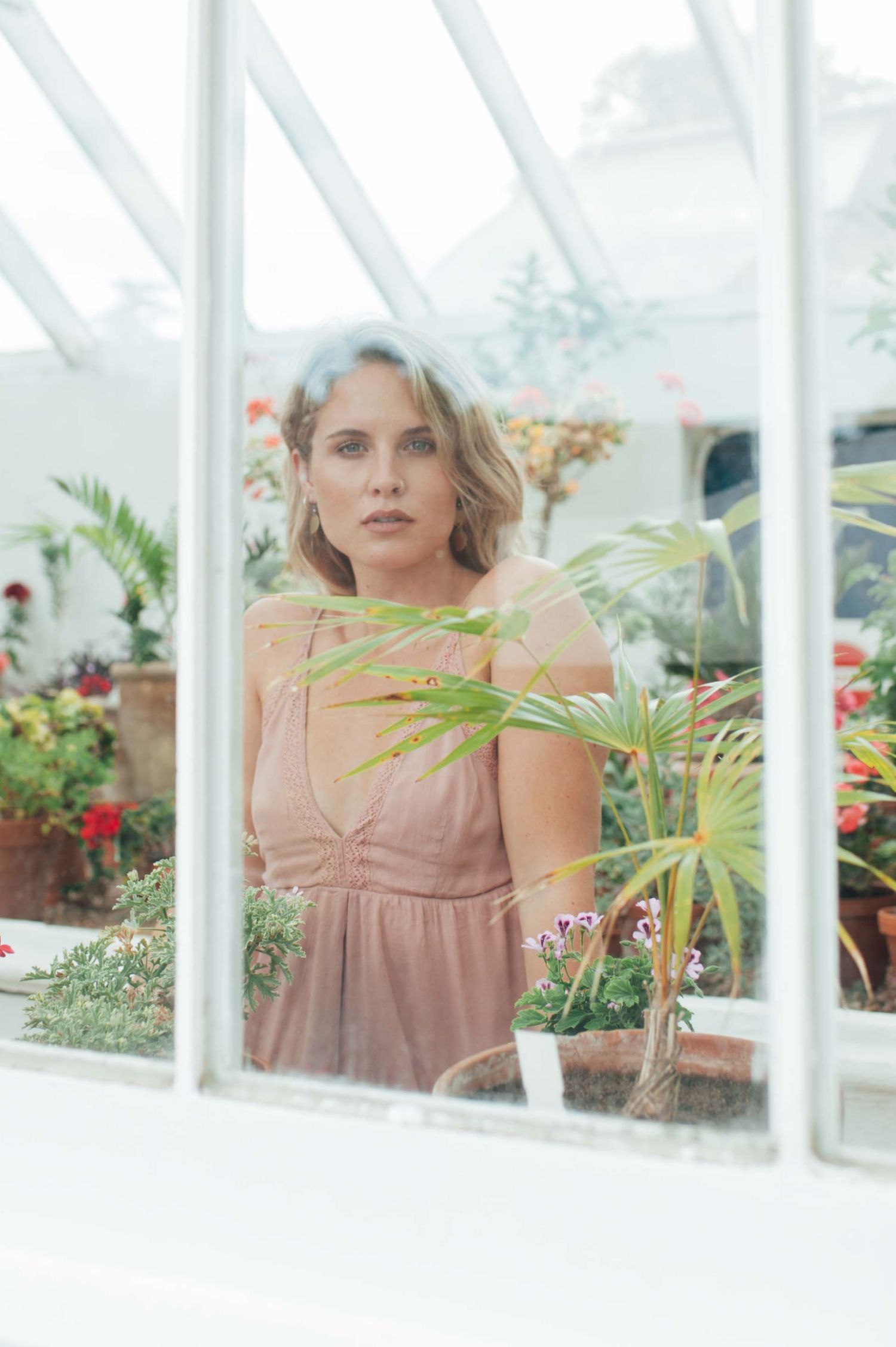 Portrait through greenhouse window with tropical plants and flowers in soft light.