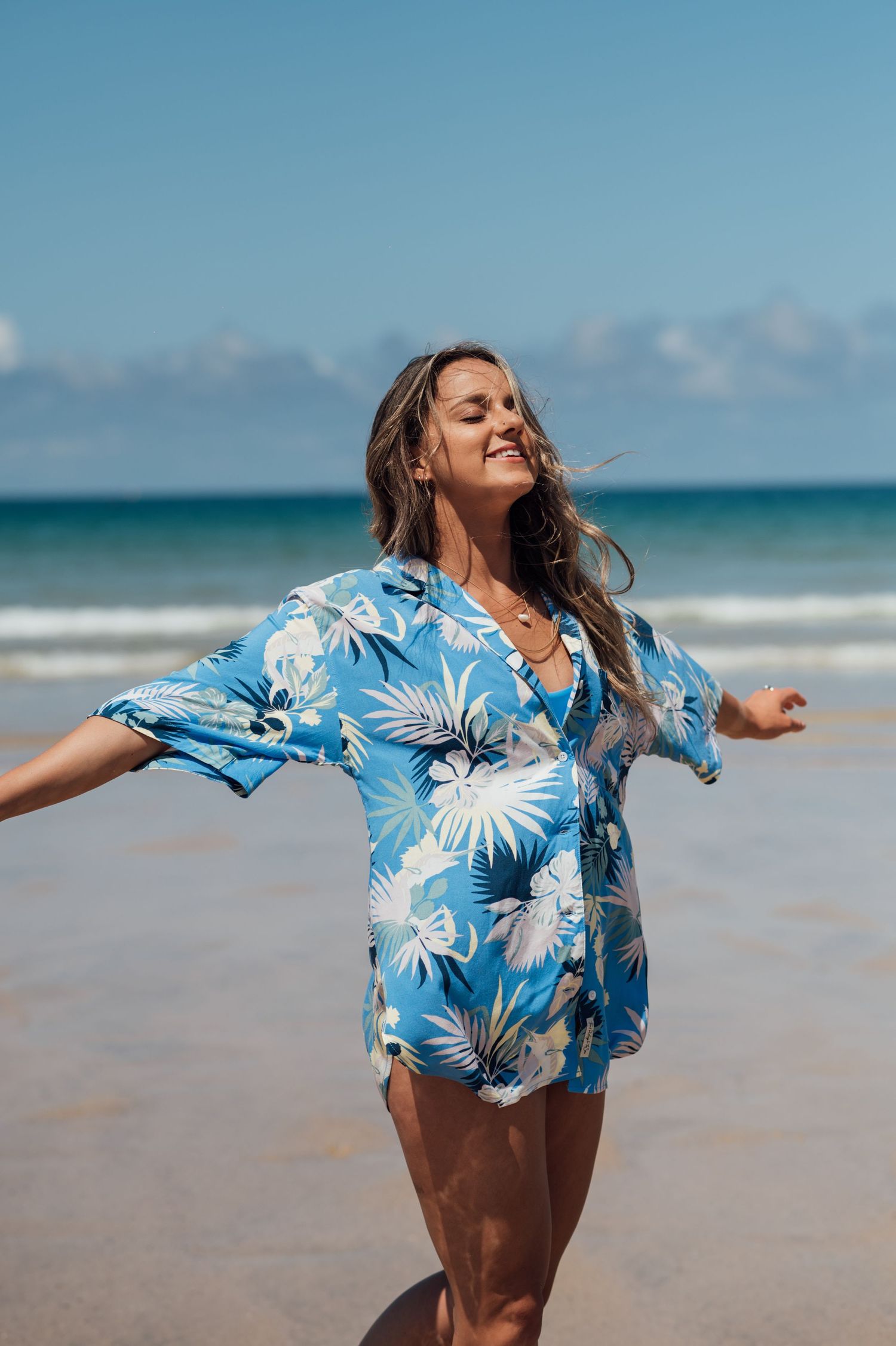 Woman in blue floral beach cover-up enjoying sunny day on tropical beach.