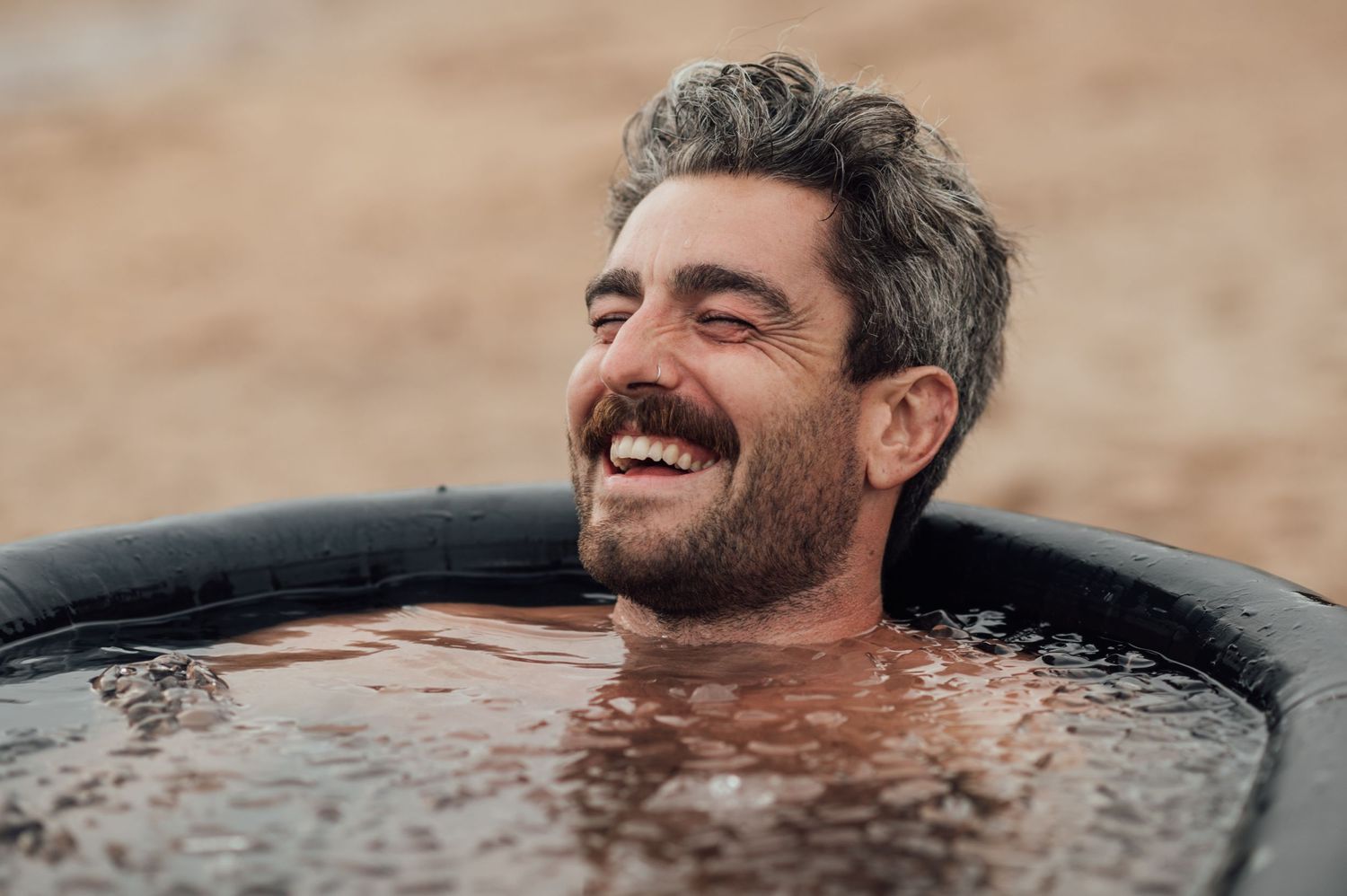 A person enjoying a relaxing soak in a dark tub while smiling.
