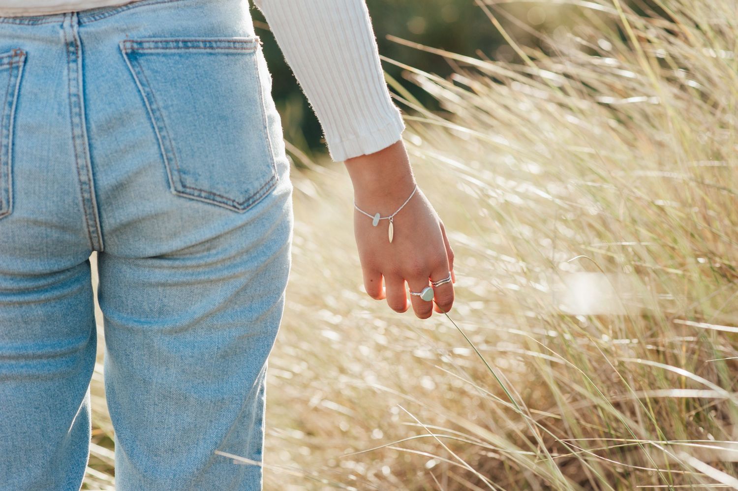Close-up shot of denim jeans and a white sweater sleeve against golden beach grass.