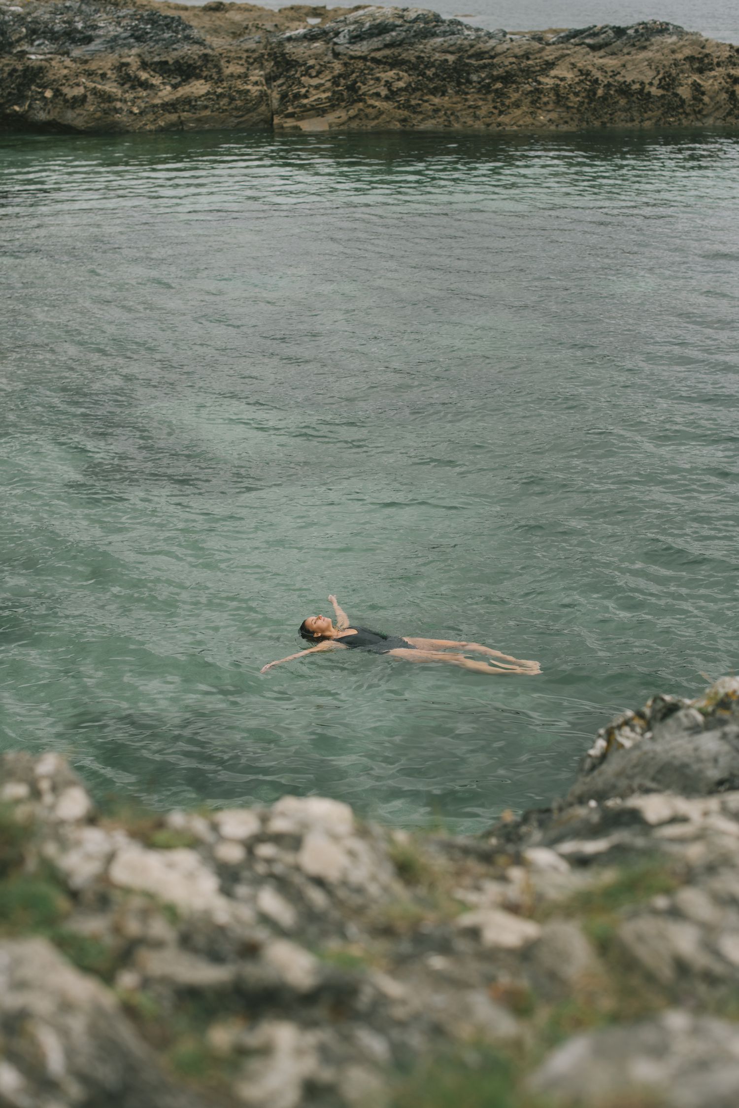 Person floating peacefully in turquoise water surrounded by rocky cliffs.