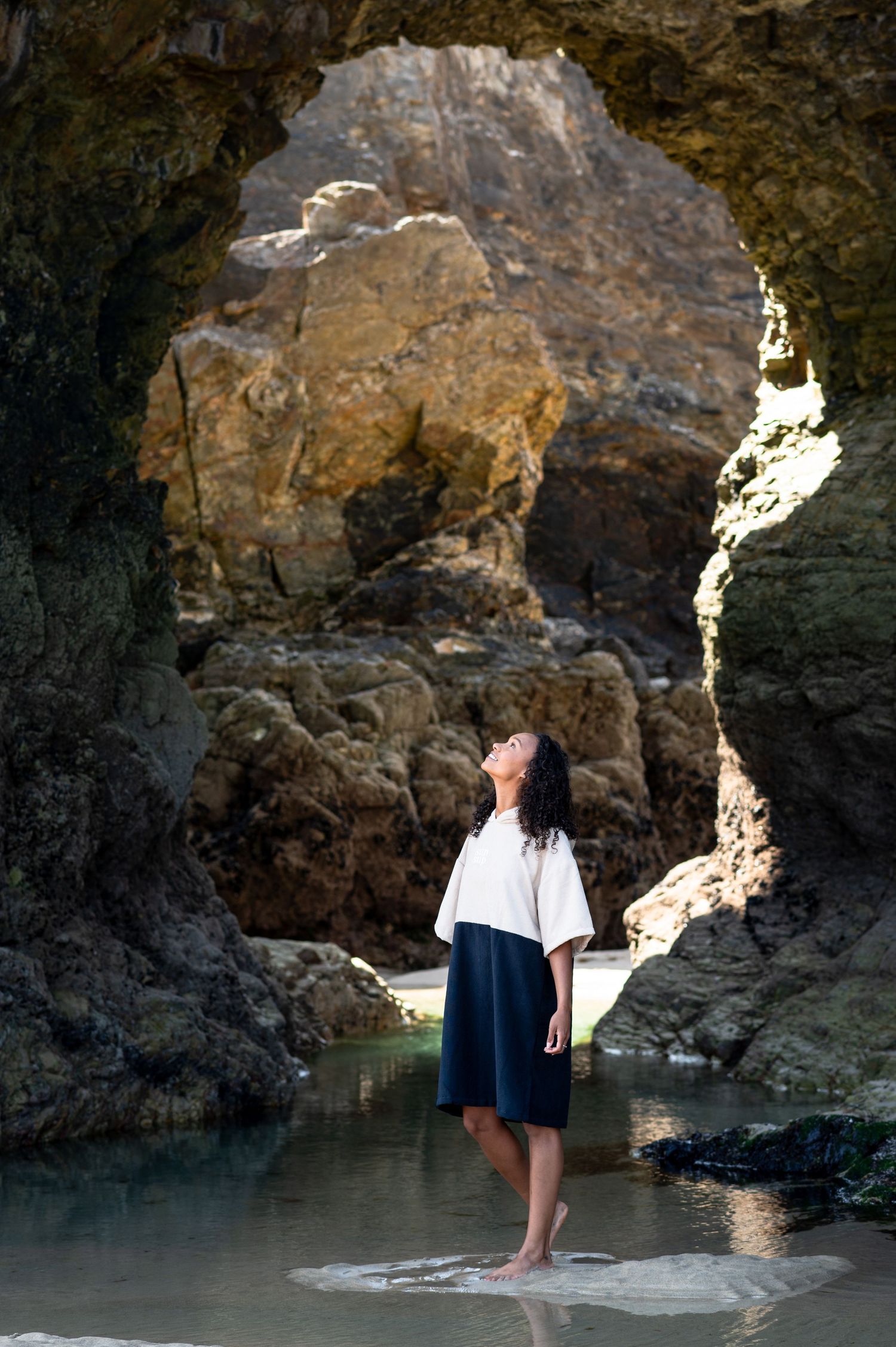 Person standing in natural rock arch cave formation by the water.
