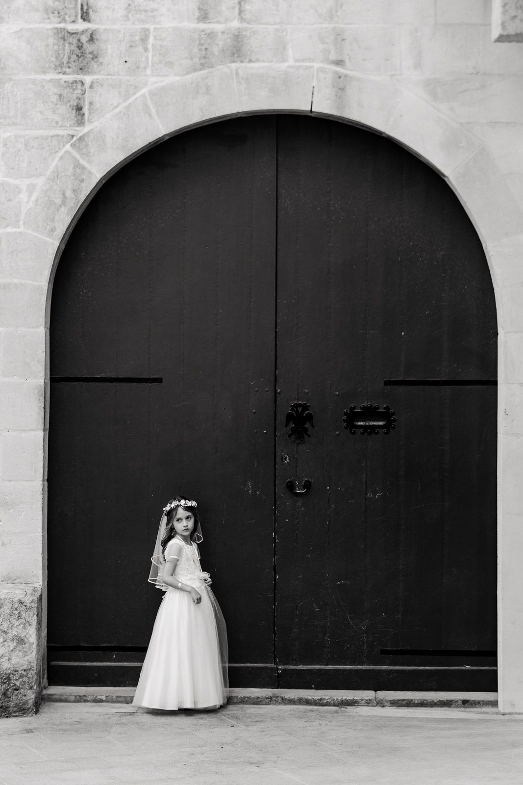 A black and white triptych shows a figure in a white dress standing against dark archways.