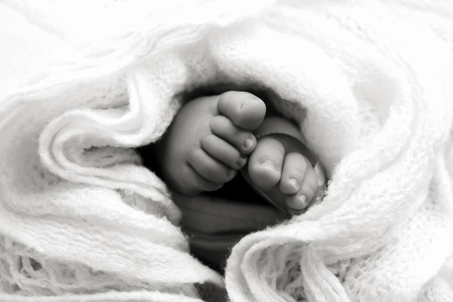 Black and white close-up of tiny baby feet wrapped in soft blanket.