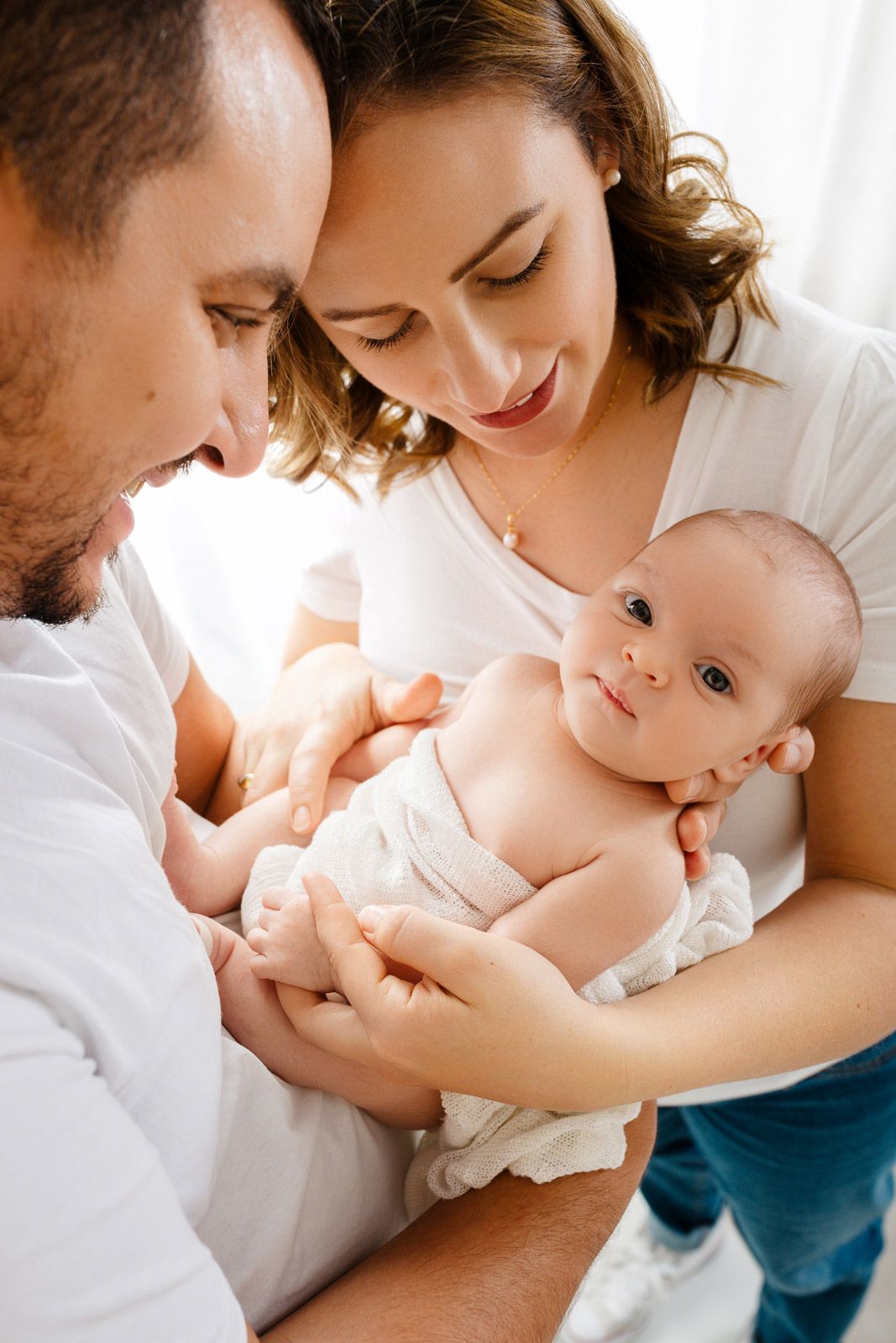 Tender family moment with baby in white clothing against bright background.