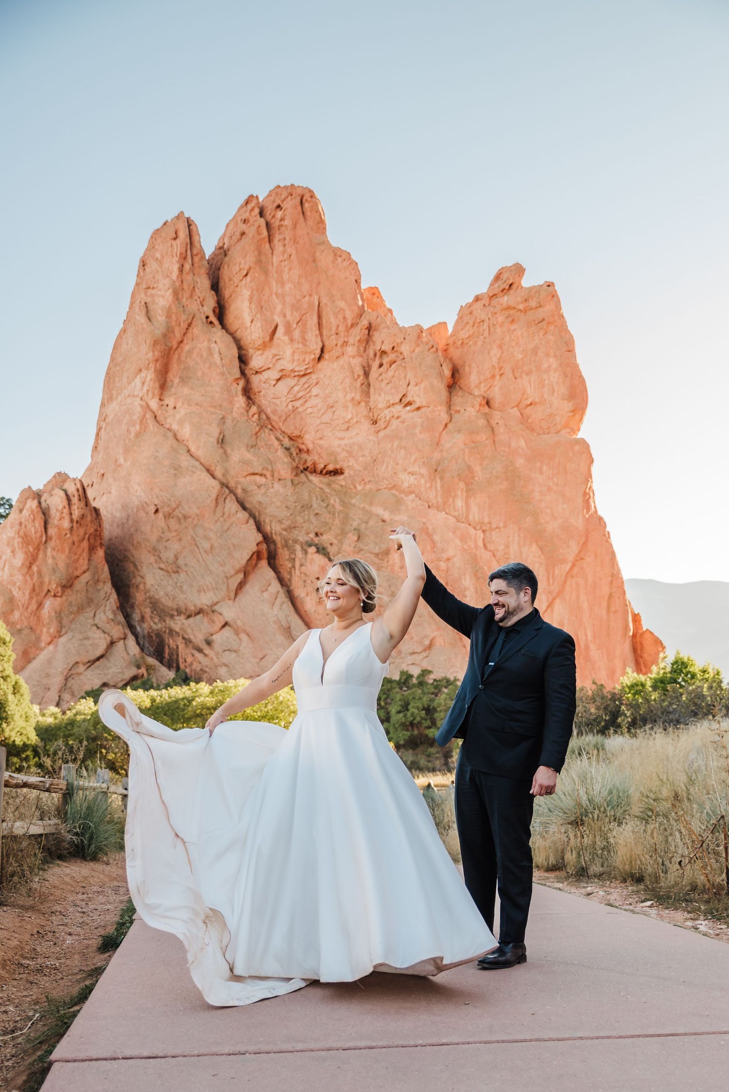 a bride and groom dancing and twirling in front of tall orange rock structures at garden of the gods in colorado springs