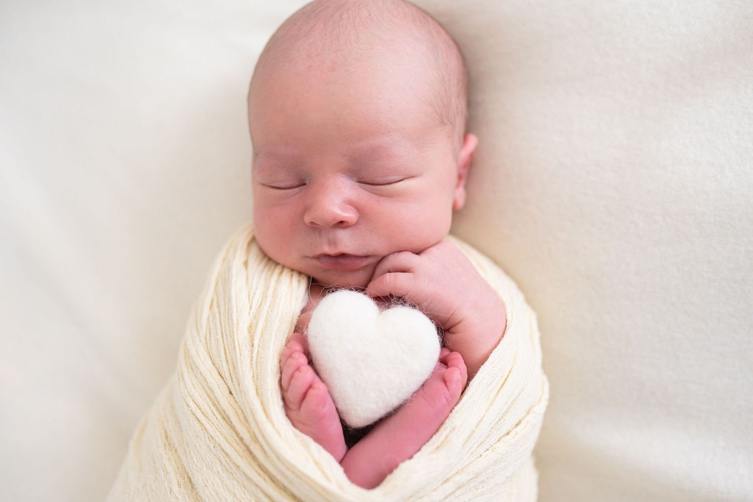 Adorable sleeping newborn baby wrapped in off-white swaddle blanket against white background.