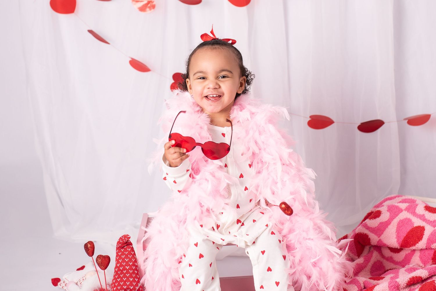 Joyful Valentine's Day scene with pink boa, red rose petals, and white backdrop for festive portrait photography.