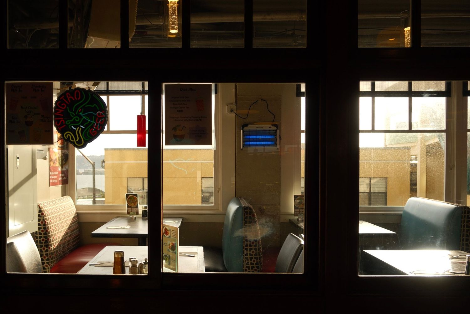 View through diner window showing retro booths, teal chairs, and warm interior lighting at night.