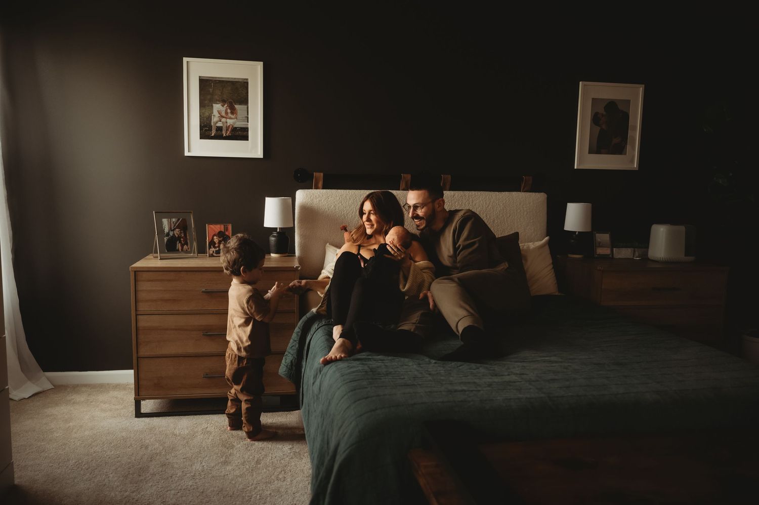 Family with young toddler sharing cozy intimate moment together on bed in dimly lit bedroom.