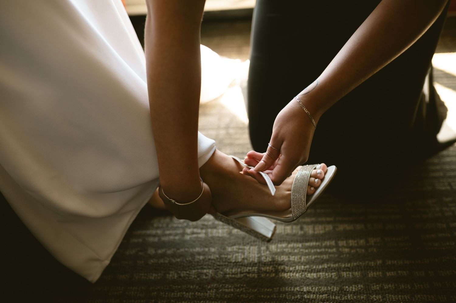 Close-up of bridal shoes being fastened on bride's feet before wedding ceremony.