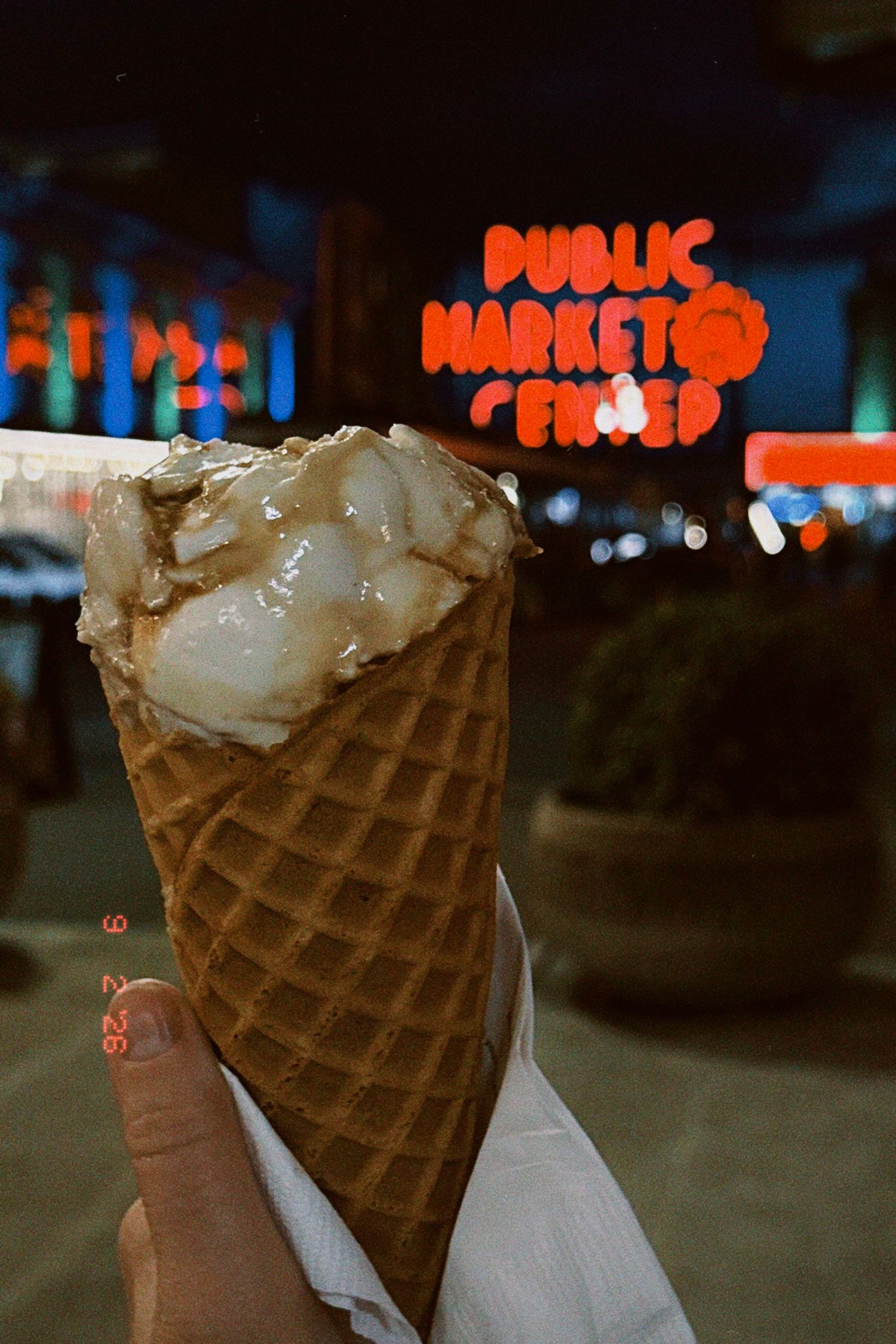 Hand holding a waffle cone with ice cream near Pike Place Public Market sign at night in Seattle.