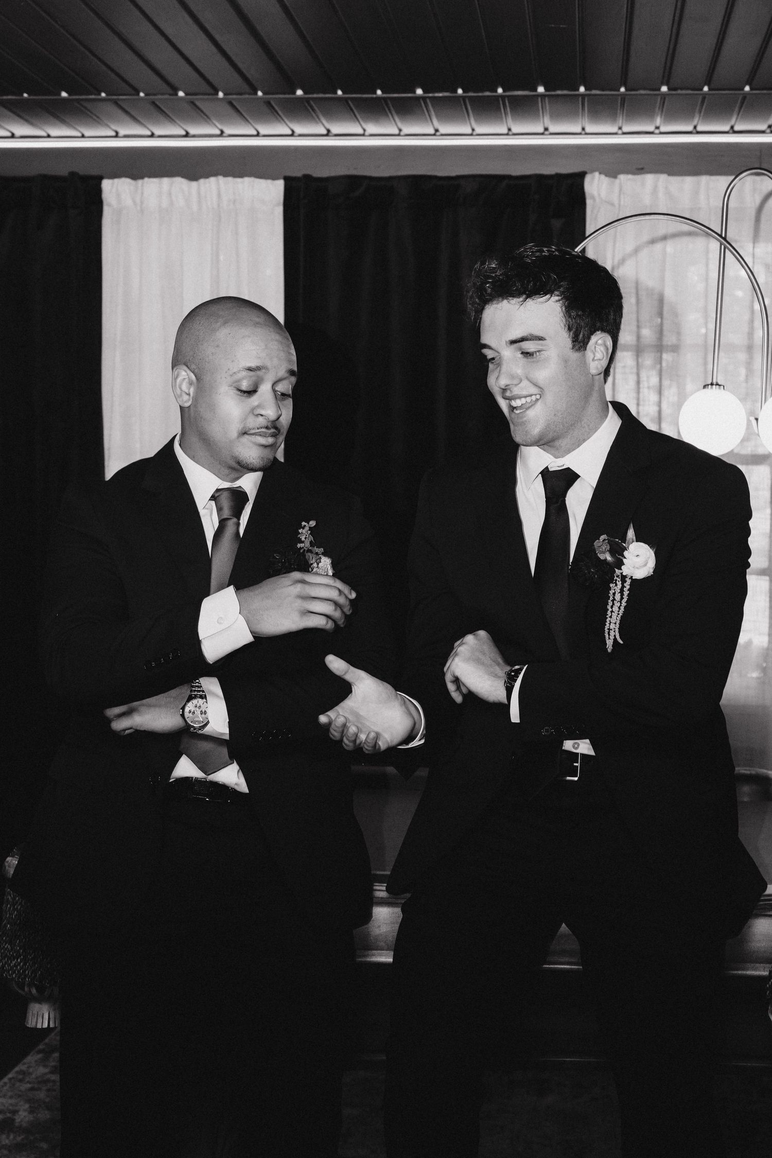 Two grooms in suits with boutonnieres share a joyful moment together at their wedding reception.