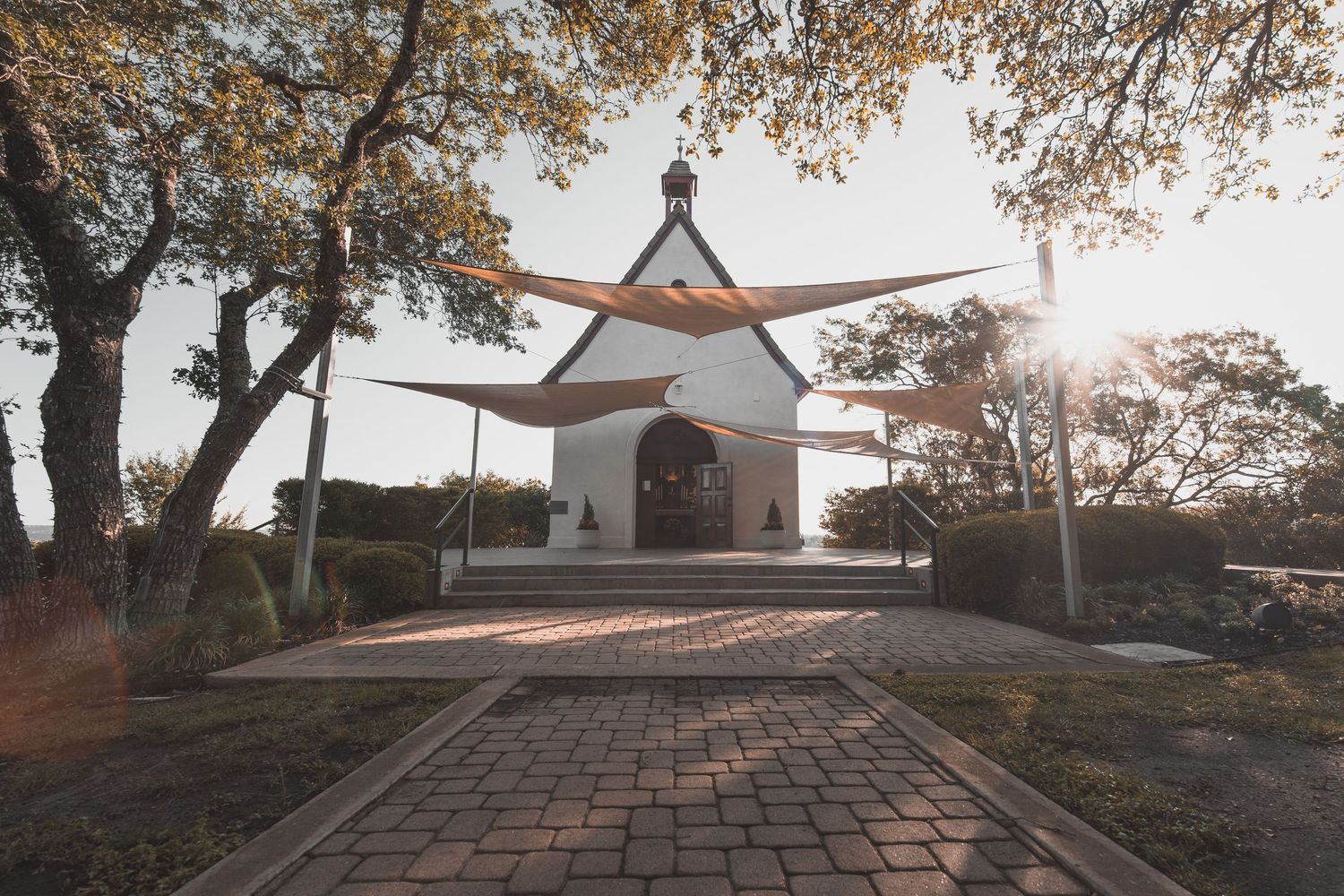 Small white chapel framed by trees and fabric canopies in warm morning sunlight Austin, Texas