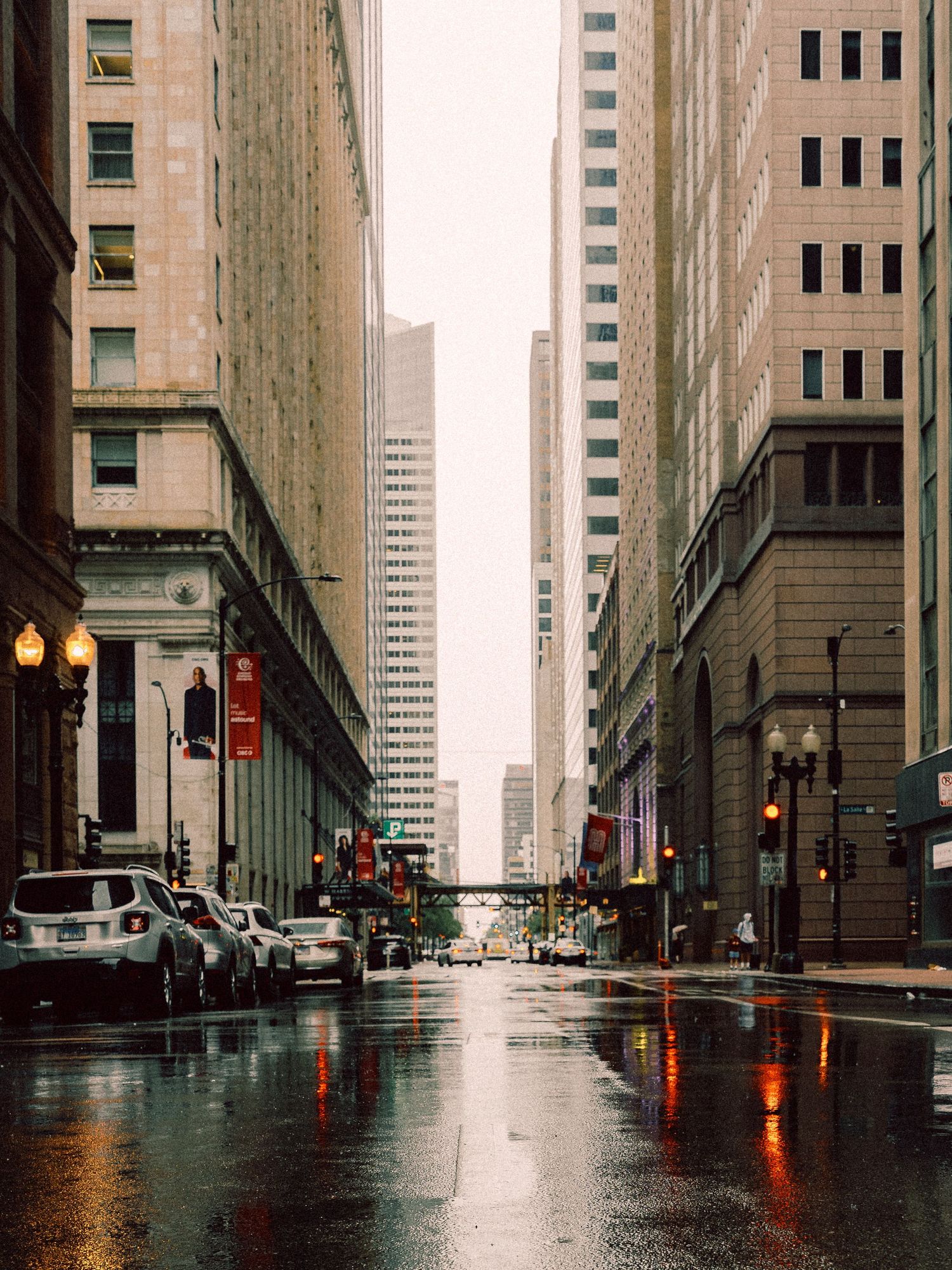 Rain-soaked street in downtown Chicago, with reflections of city lights and tall buildings framing the roadway.