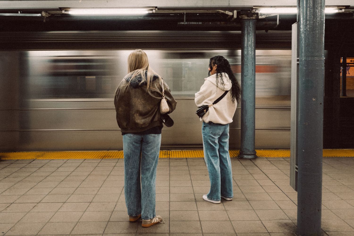 Two passengers waiting on a New York City subway platform as a train passes