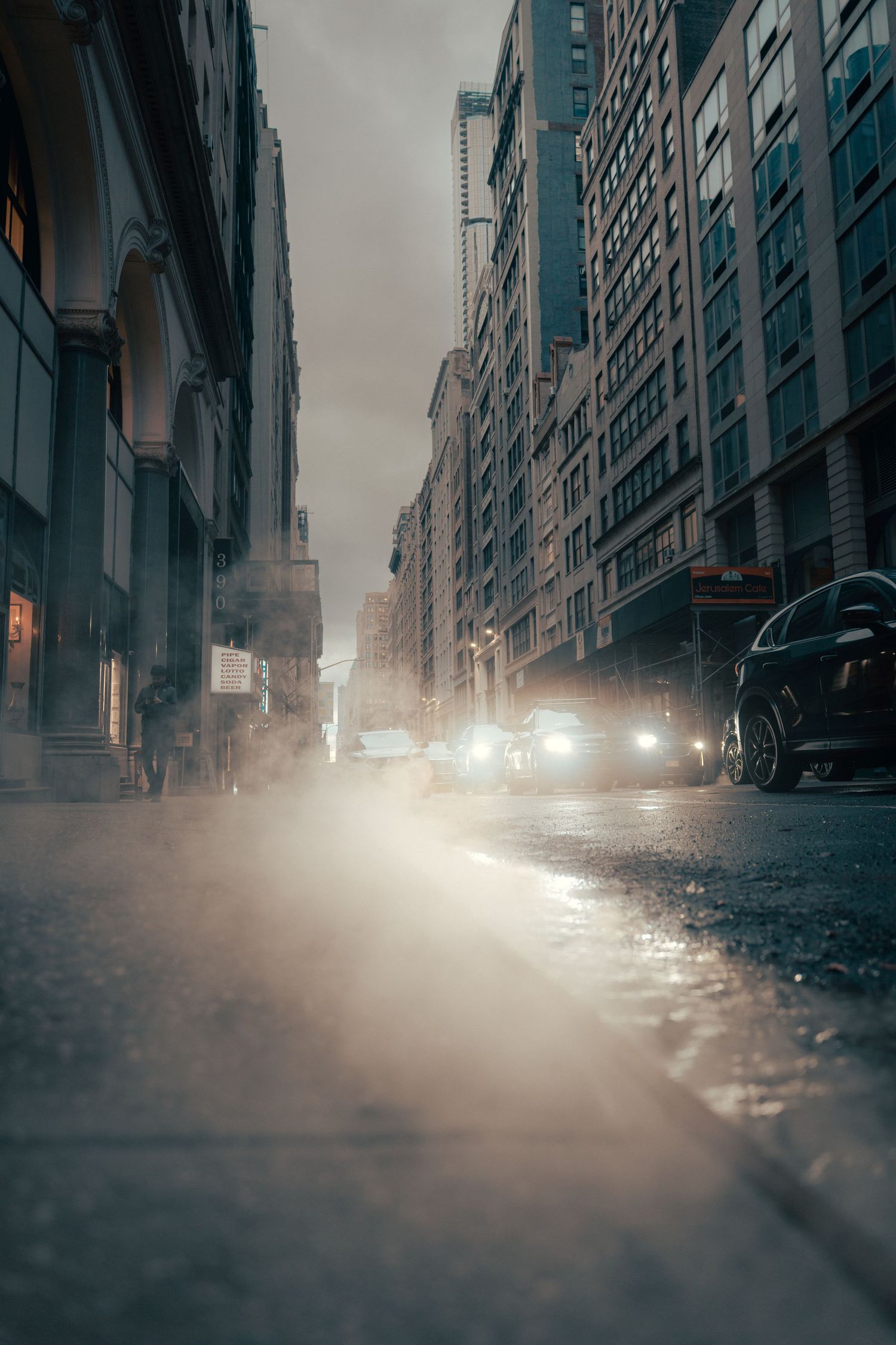 Early evening street scene with headlights and steam in Manhattan, New York City