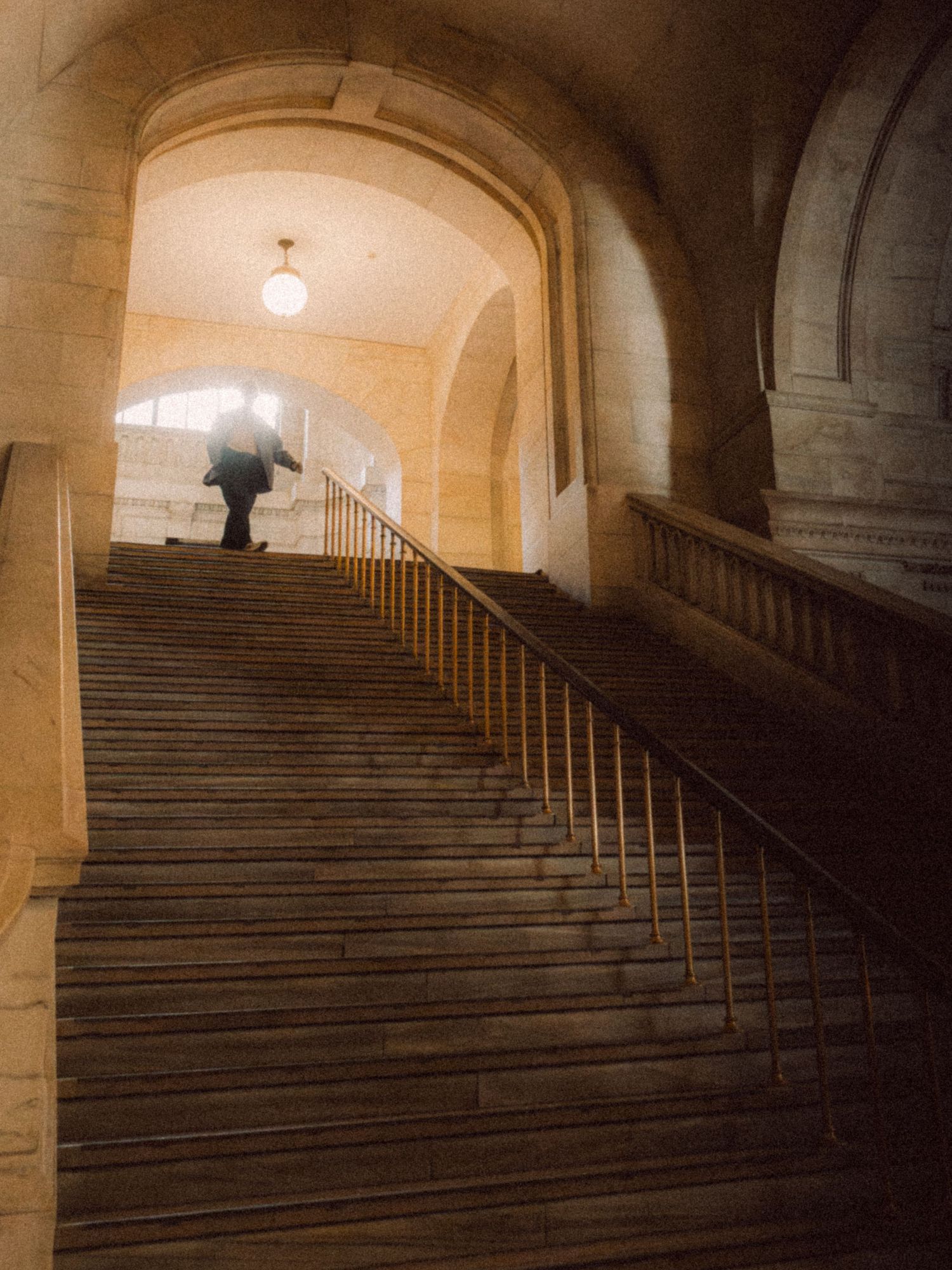 Person ascending a grand stone staircase beneath an arched passageway