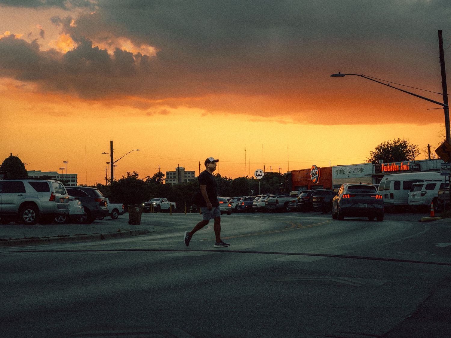 Pedestrian crossing a North Loop street in Austin, Texas beneath a dramatic late golden-hour sky