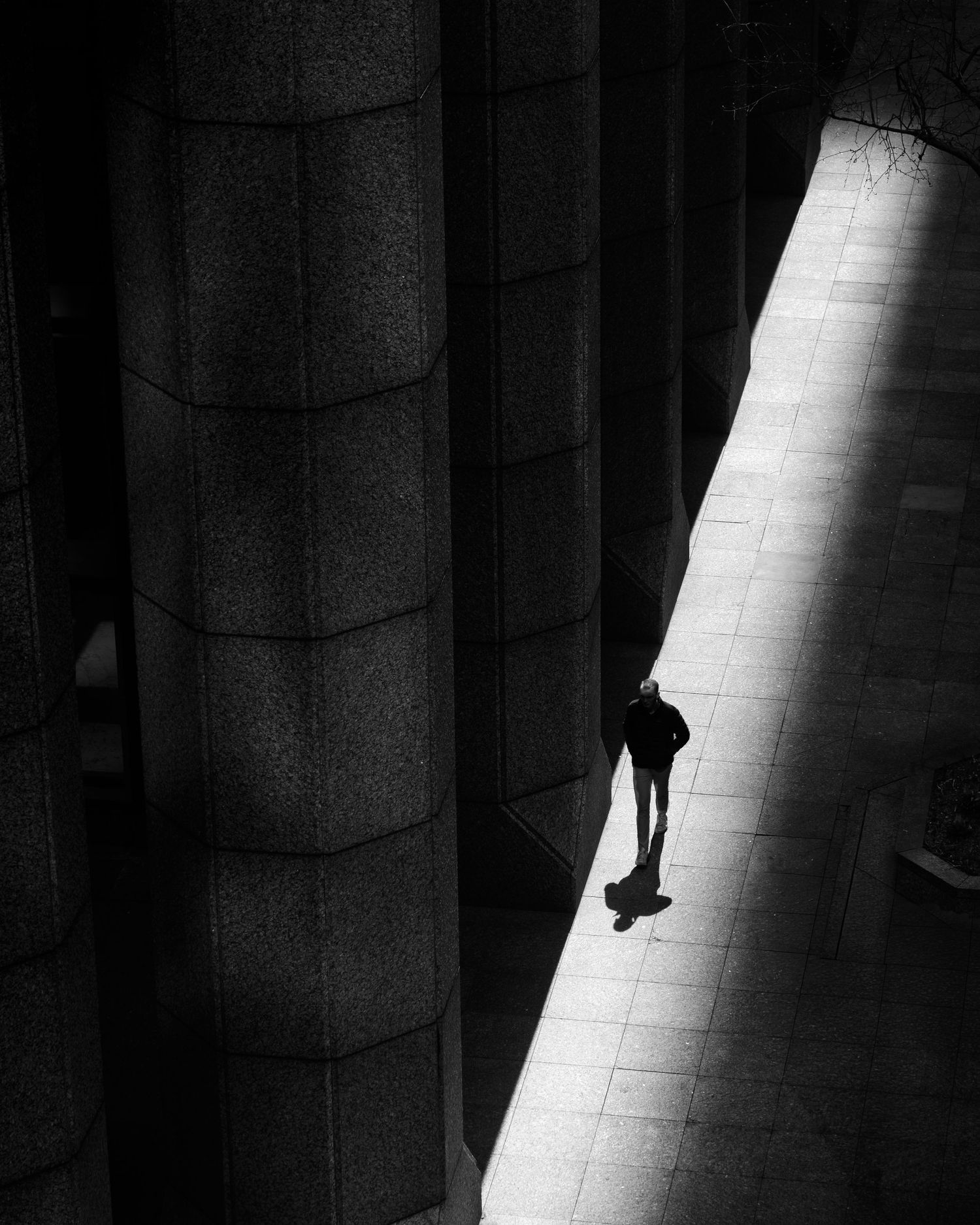 Black and white street photograph of a lone pedestrian crossing a shaft of light in Manhattan