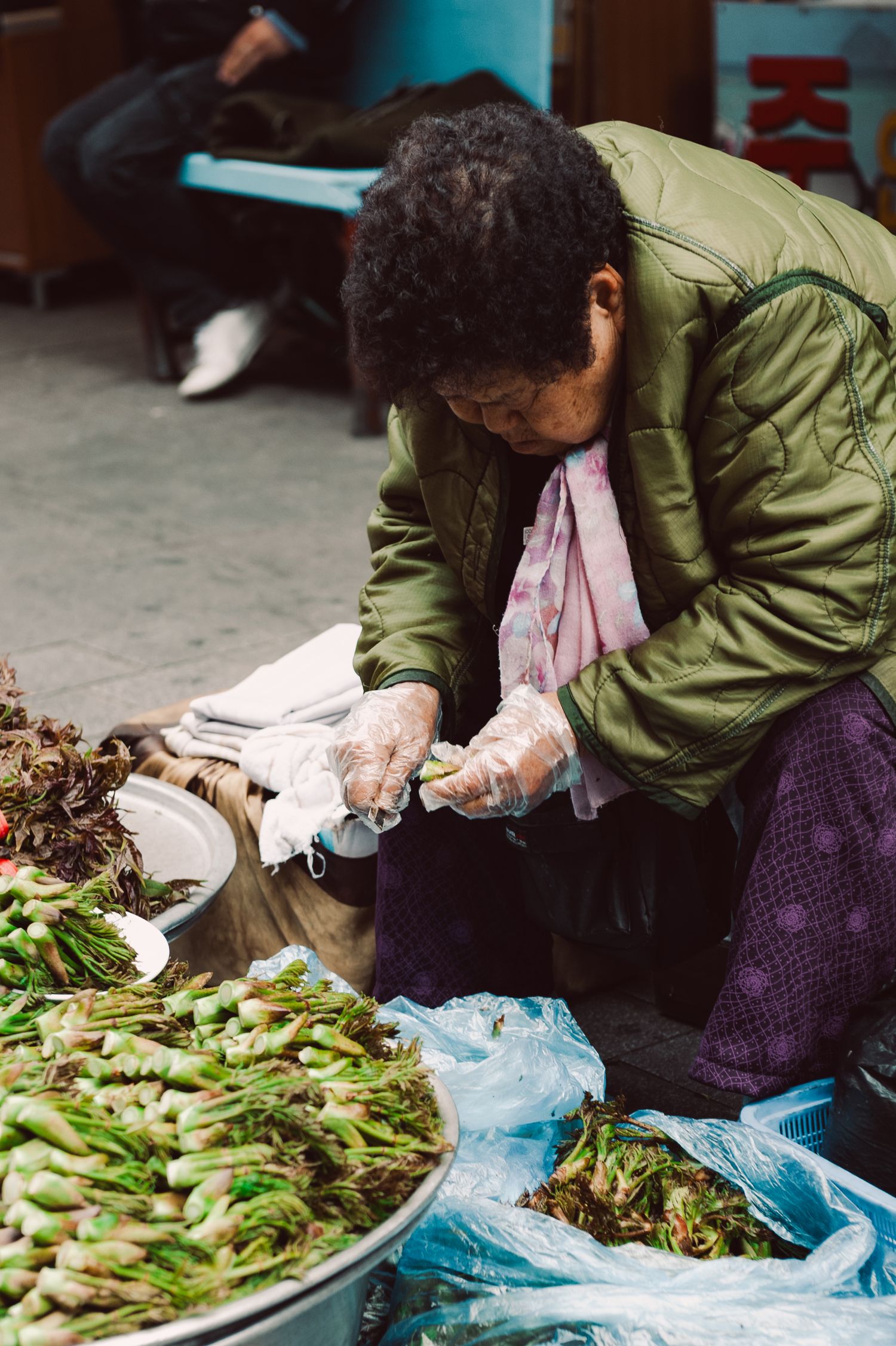 A vendor preparing fresh produce at a traditional Korean street market, surrounded by baskets of vegetables.  Seoul, South Korea.