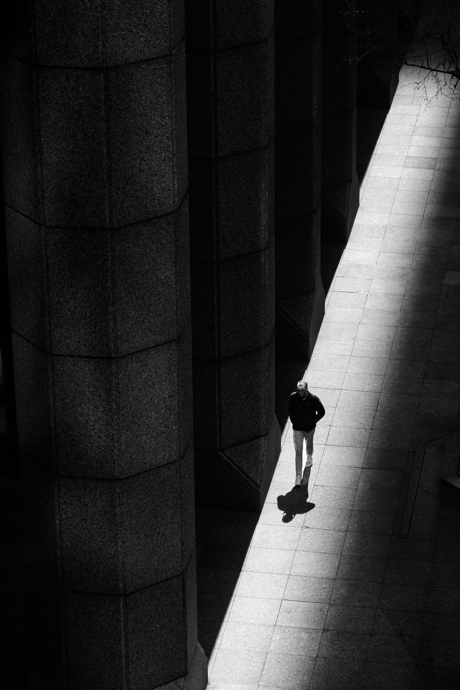Black and white street photograph of a lone pedestrian crossing a shaft of light in Manhattan, New York City