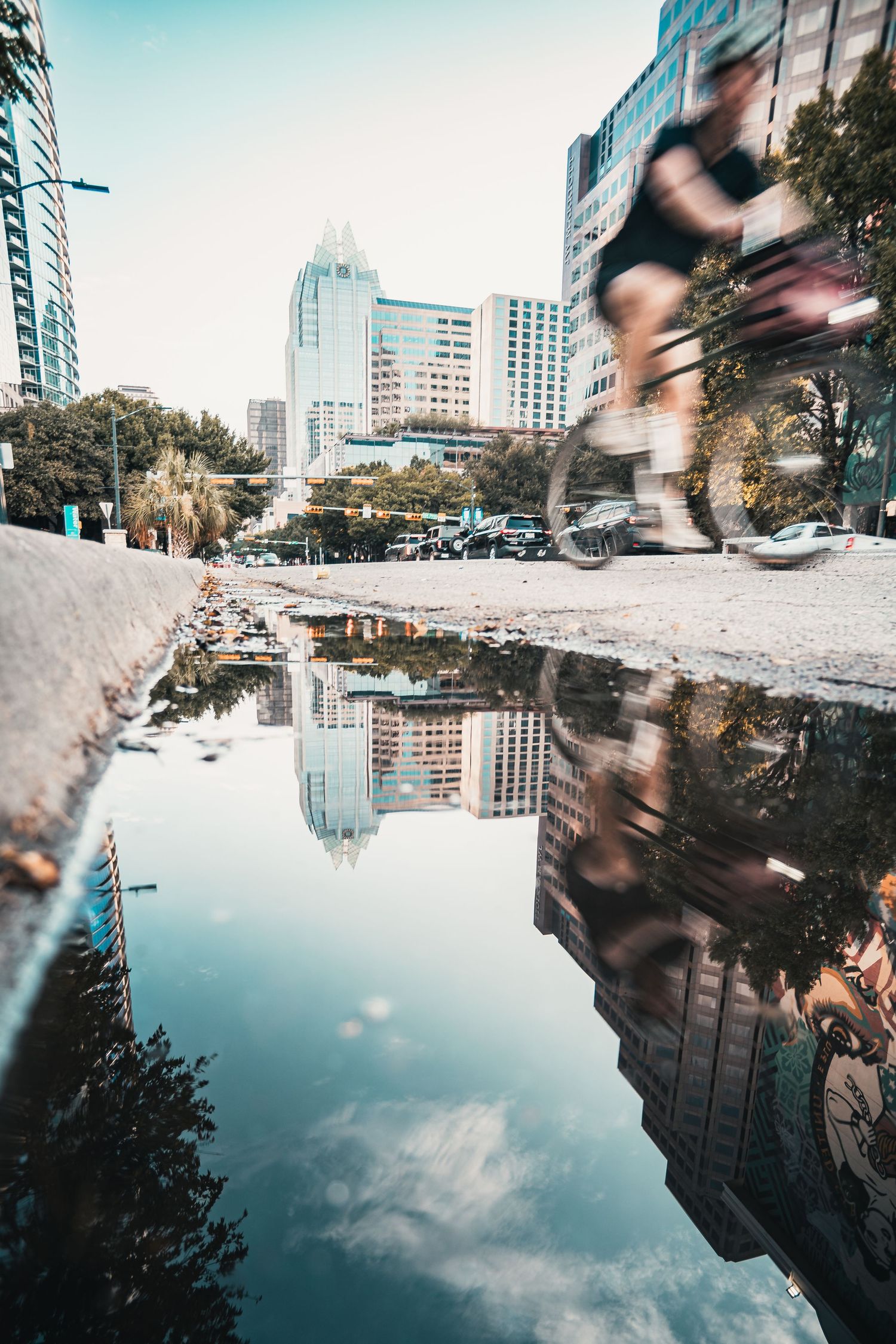 Cyclist crossing Congress Avenue Bridge with the downtown Austin skyline reflected in a puddle