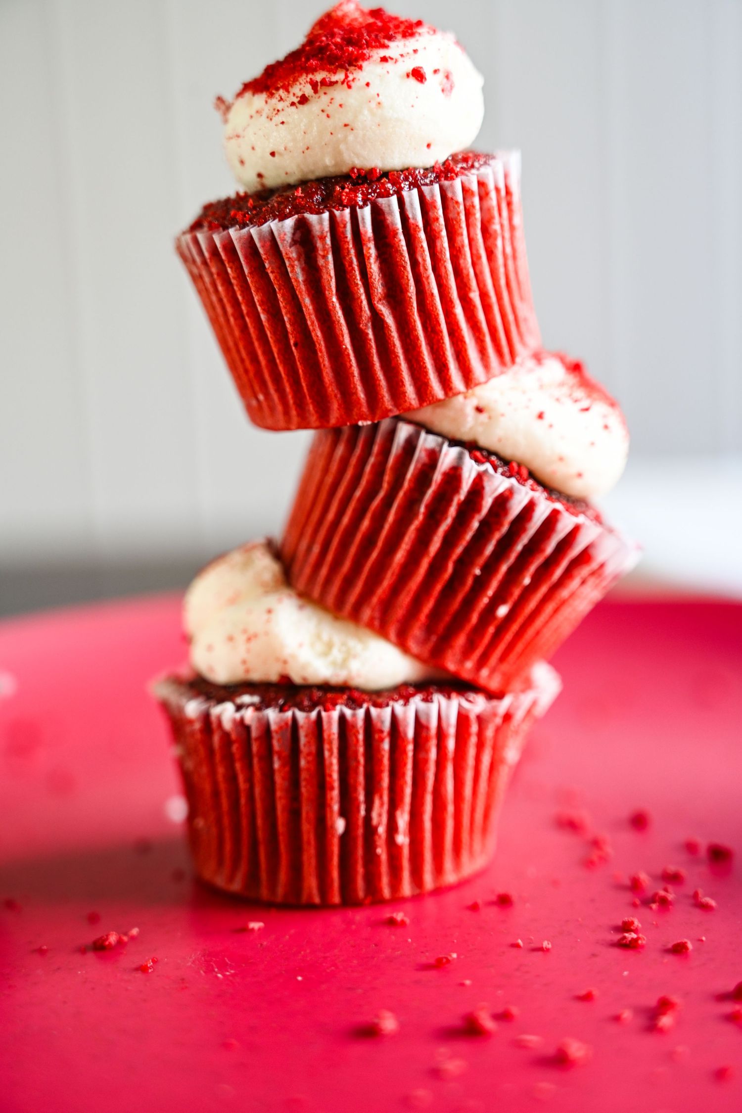 Stack of three red velvet cupcakes with cream cheese frosting on a red plate.