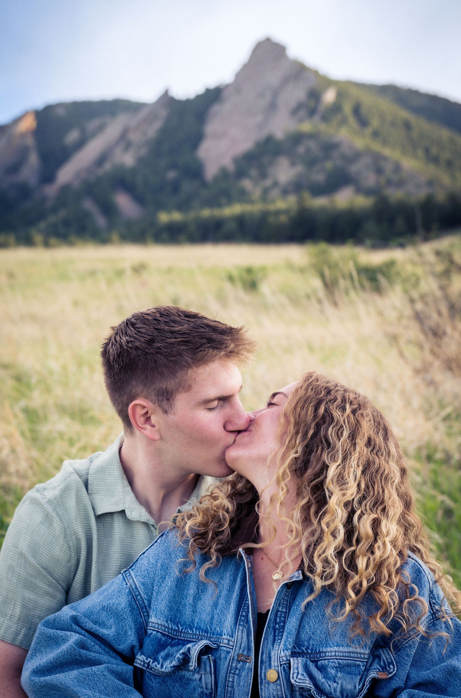 Couple sharing a romantic kiss in a grassy field with the Flatirons mountains in the background.