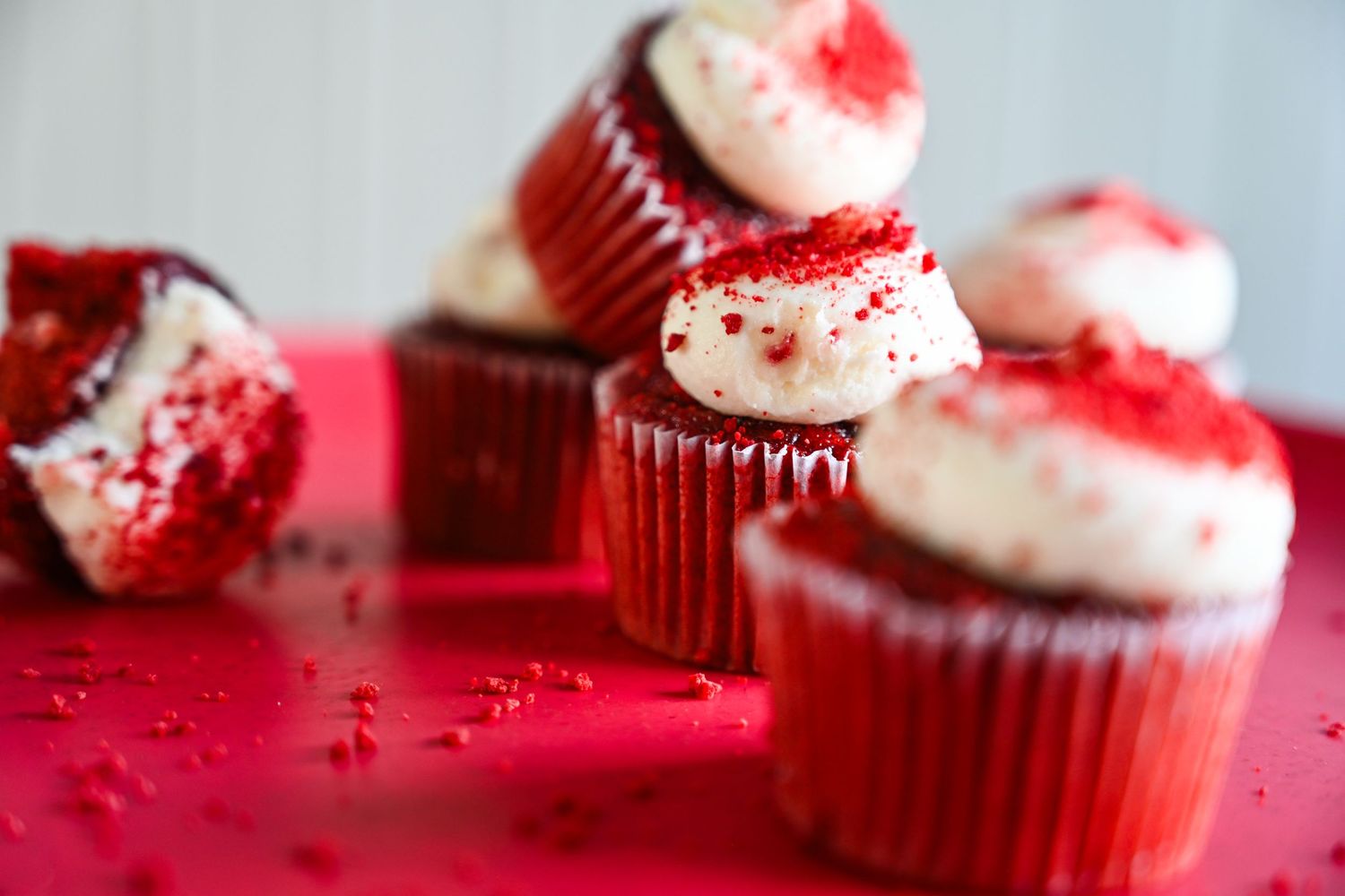 Red velvet cupcakes with white cream cheese frosting and red crumble on a red surface.