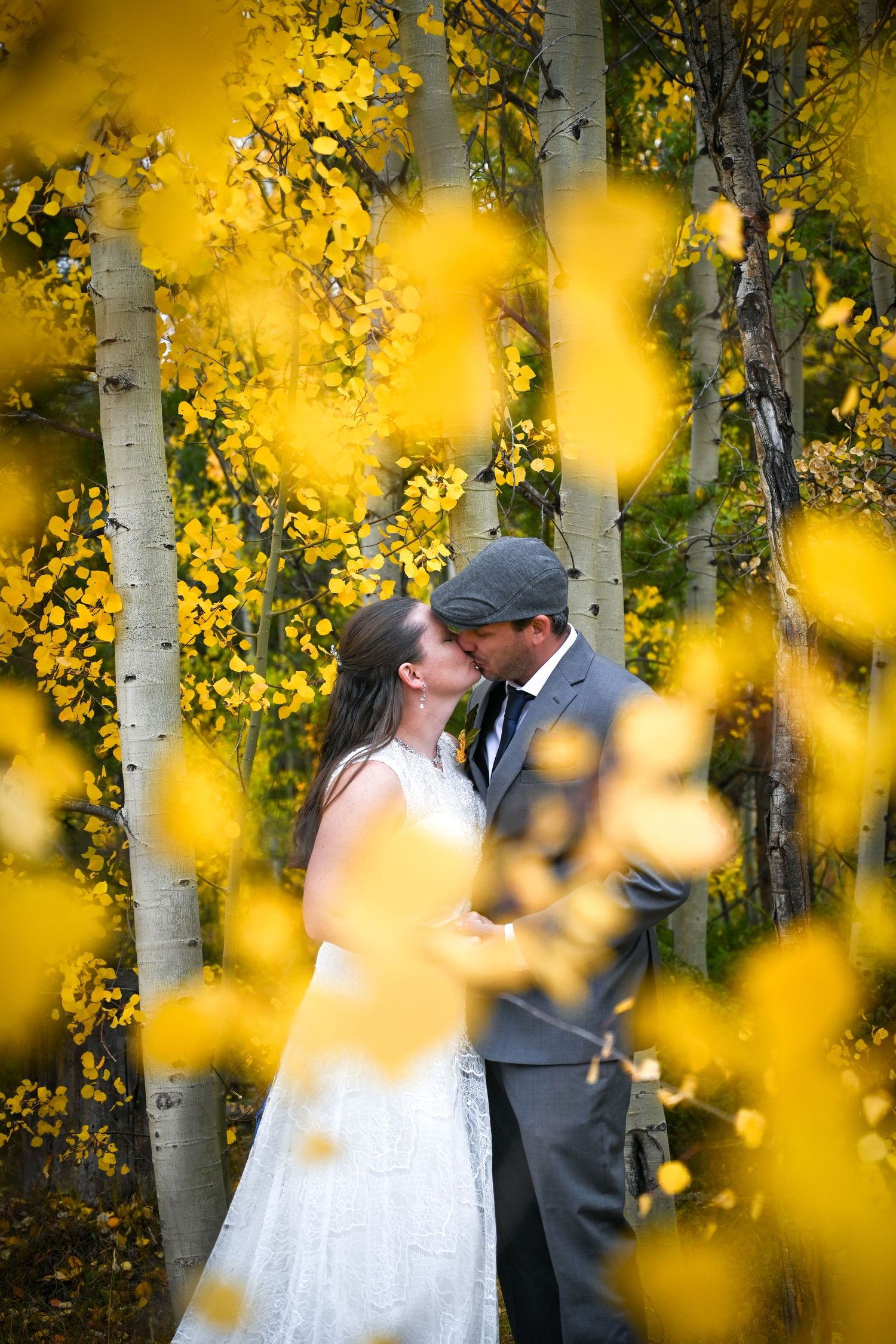 Newlyweds sharing a kiss framed by golden yellow aspen trees in fall foliage.
