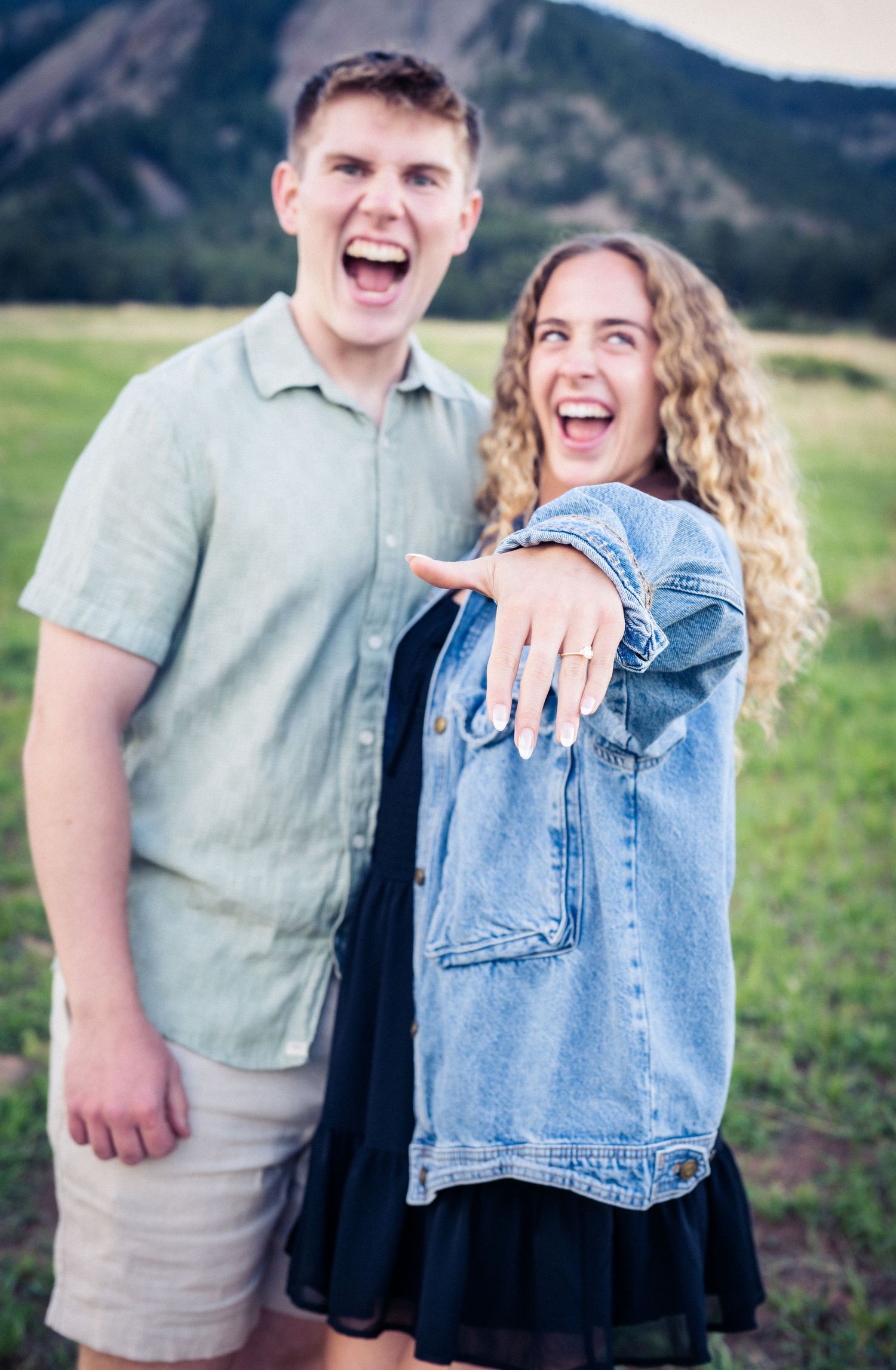 Excited couple showing off engagement ring outdoors with rocky mountain flatirons backdrop.