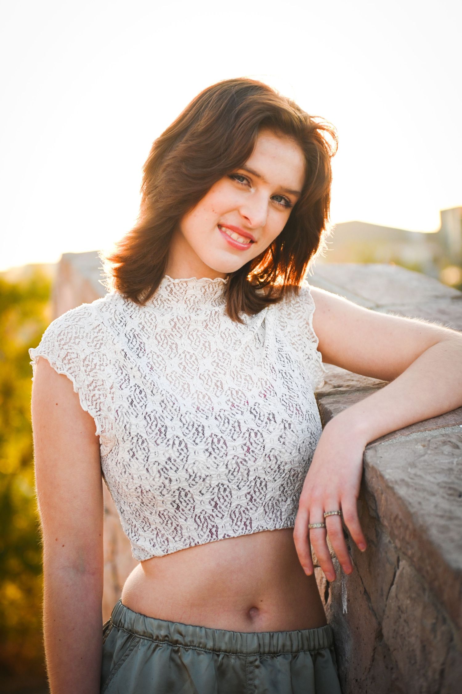 Young brunette woman in white lace crop top smiling warmly in golden sunset light.