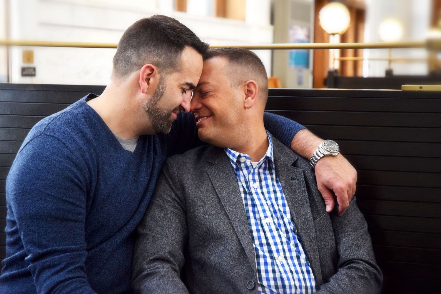 Two men sharing a tender romantic moment together seated on a bench during an engagement photo session.