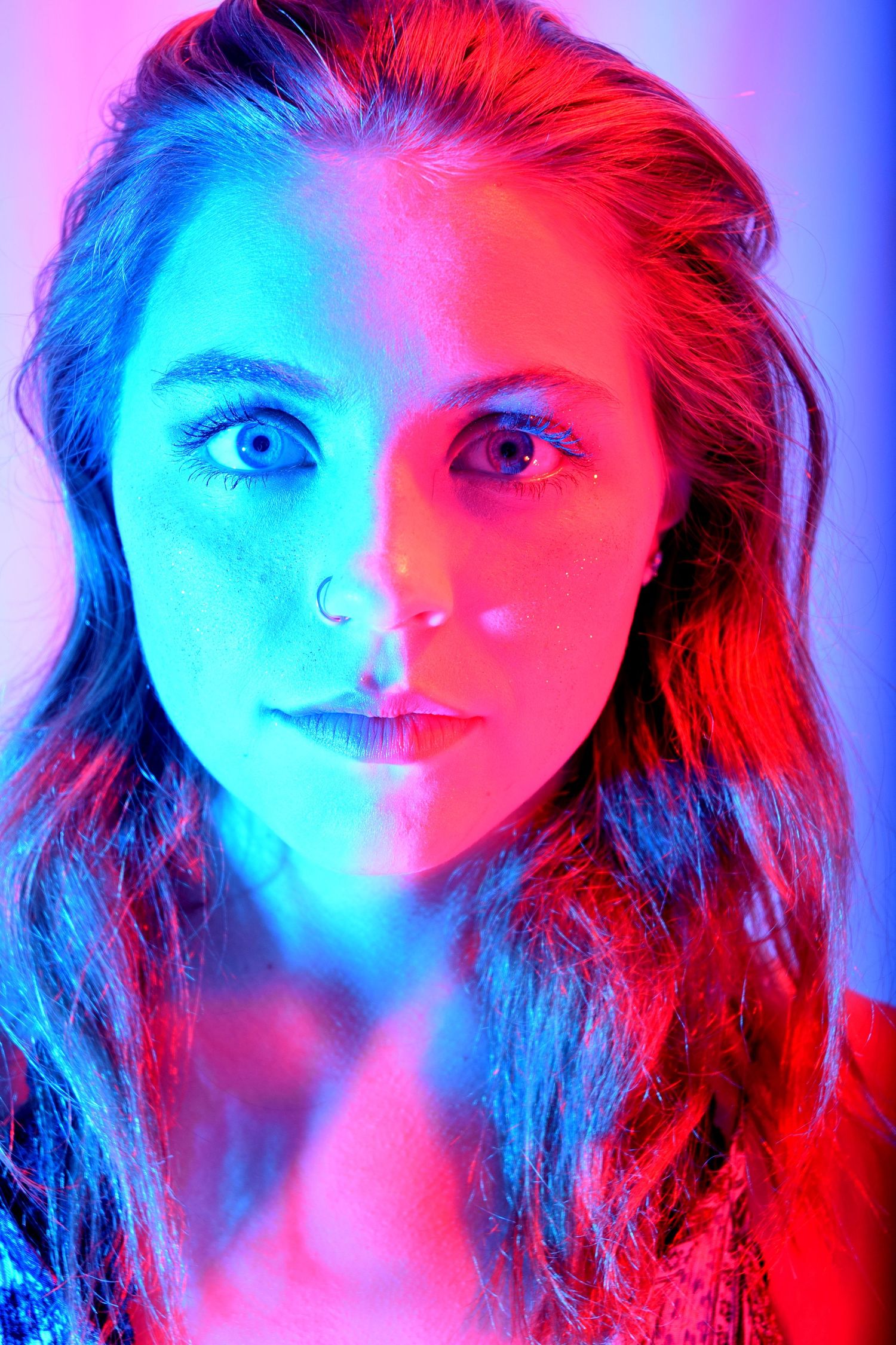 Portrait of a young woman illuminated by split blue and red neon lighting, creating a dramatic dual-tone effect.