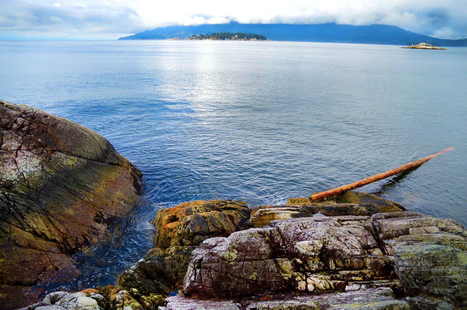 Rocky shoreline with orange kayak, calm blue ocean waters, and misty mountain island in background.