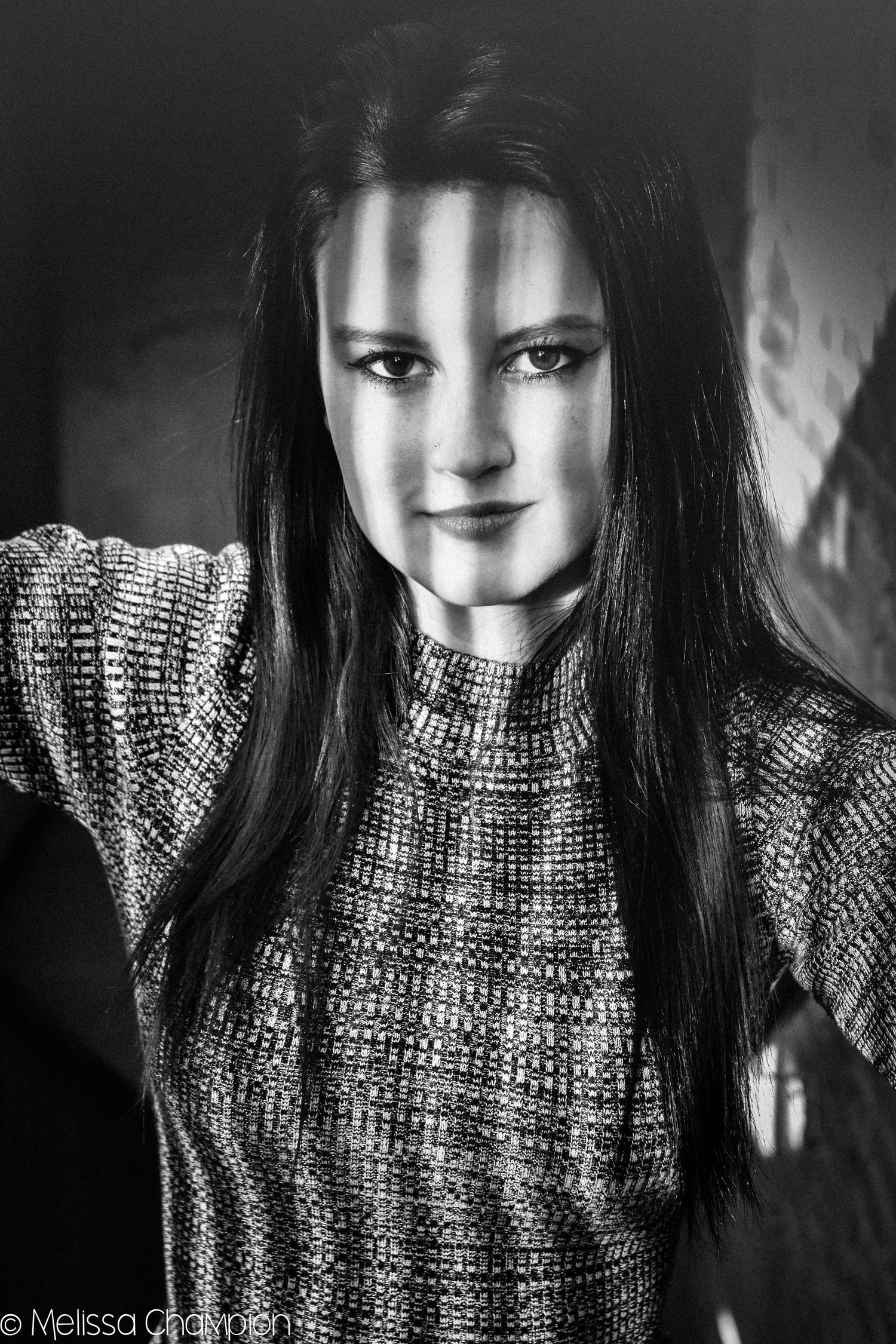 Black and white portrait of a young woman with long dark hair wearing a knit sweater, dramatic light and shadow.