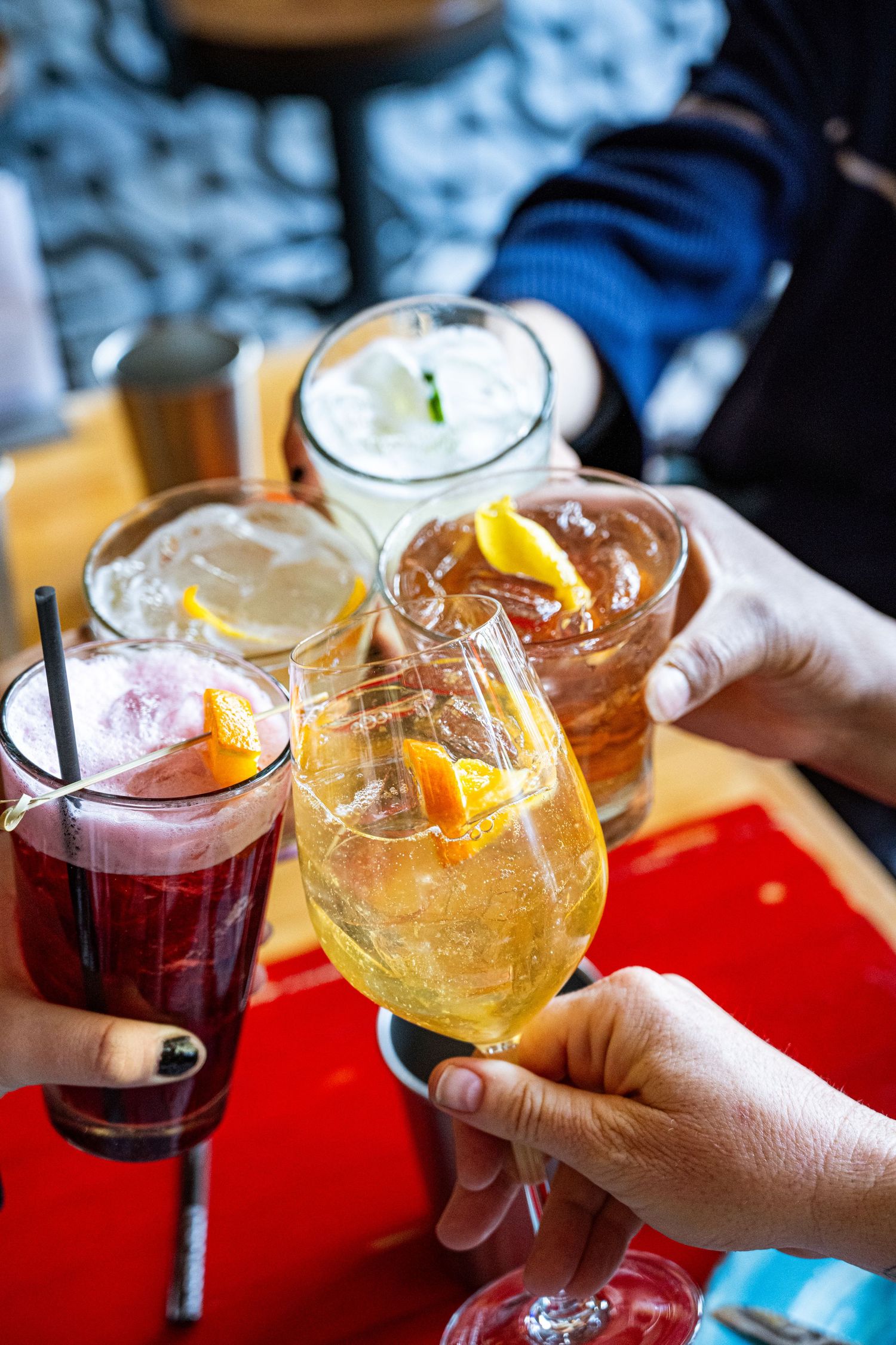 Friends toasting with colorful cocktails including an Aperol spritz and red berry drinks.