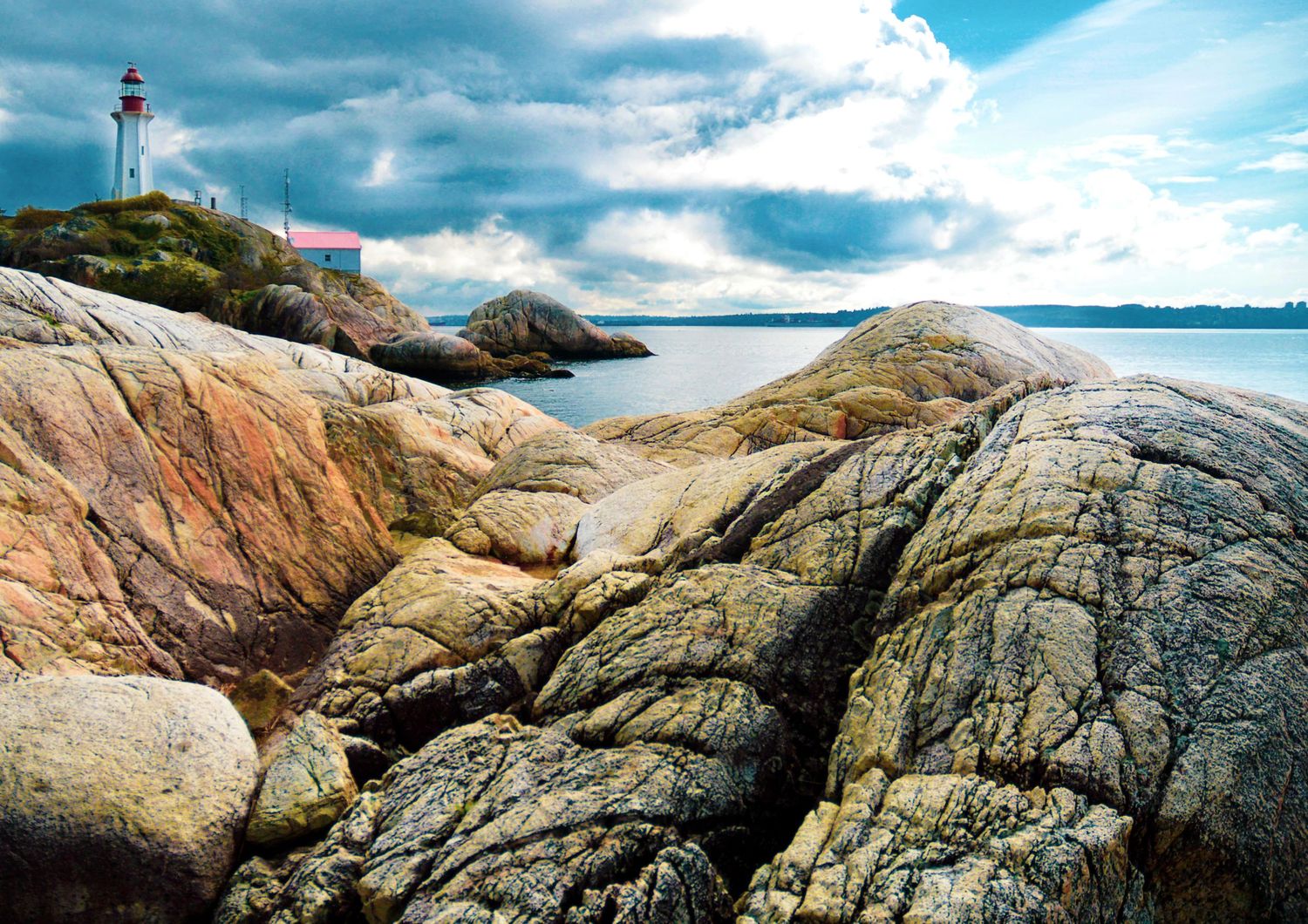 Rocky coastal landscape with a white lighthouse on a small island under dramatic cloudy skies by the sea.