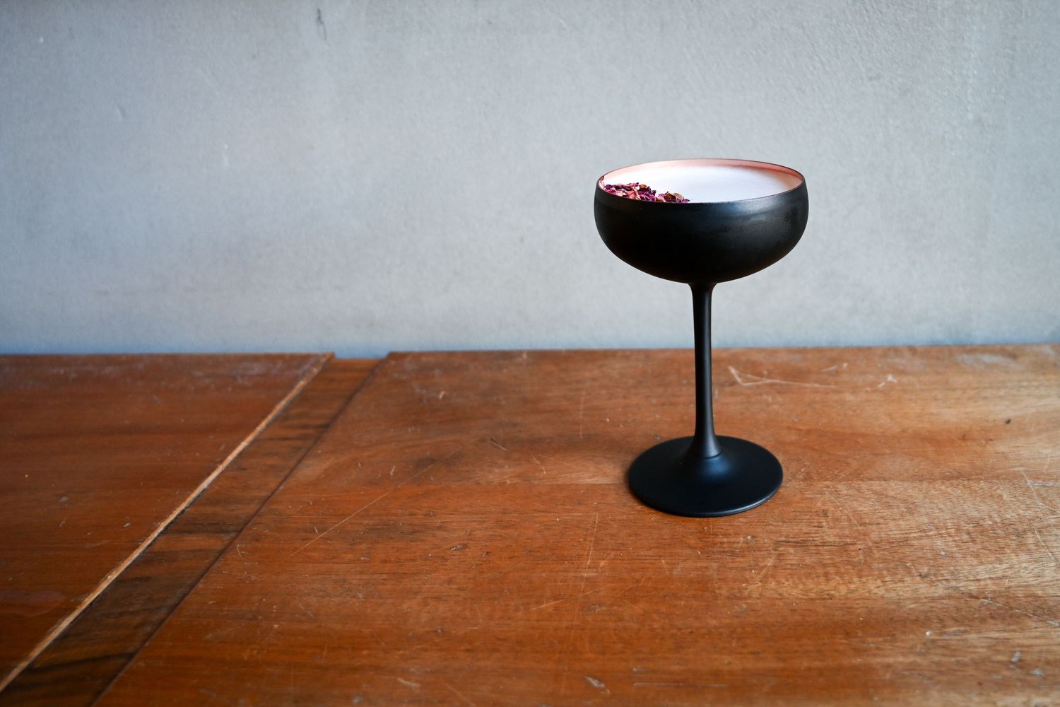 Elegant black coupe glass with a creamy cocktail garnished with red berries on a wooden table.