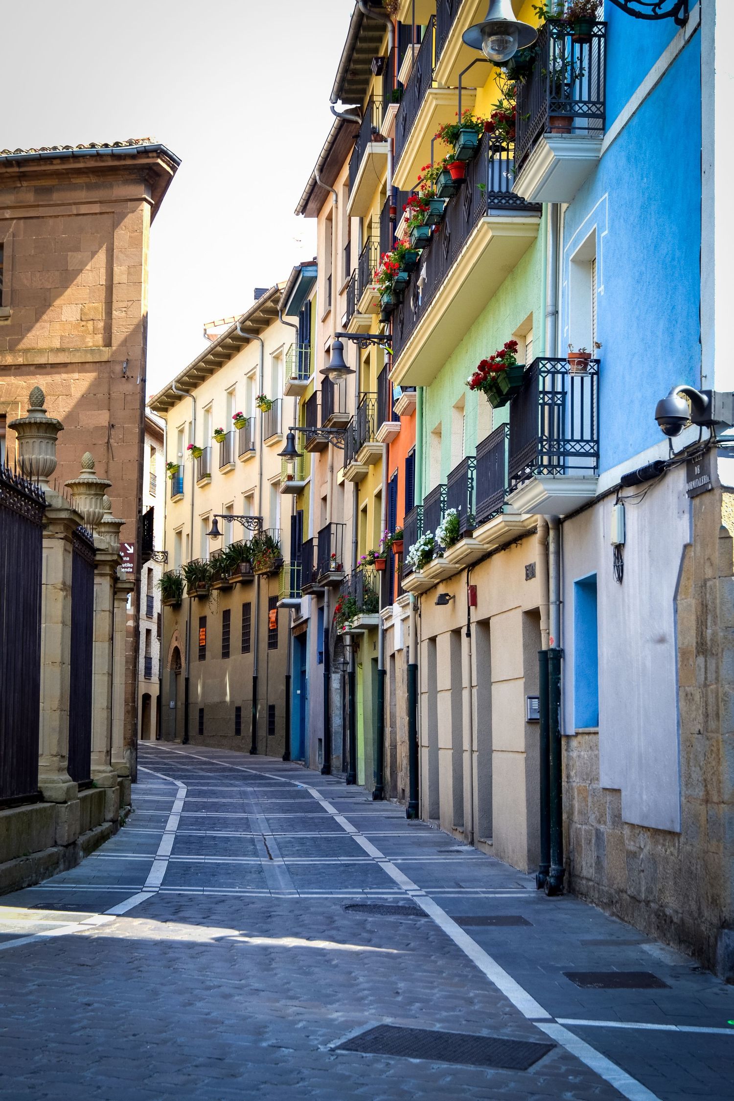 Colorful narrow cobblestone street lined with vibrant buildings and flower-adorned balconies in a charming European old town.
