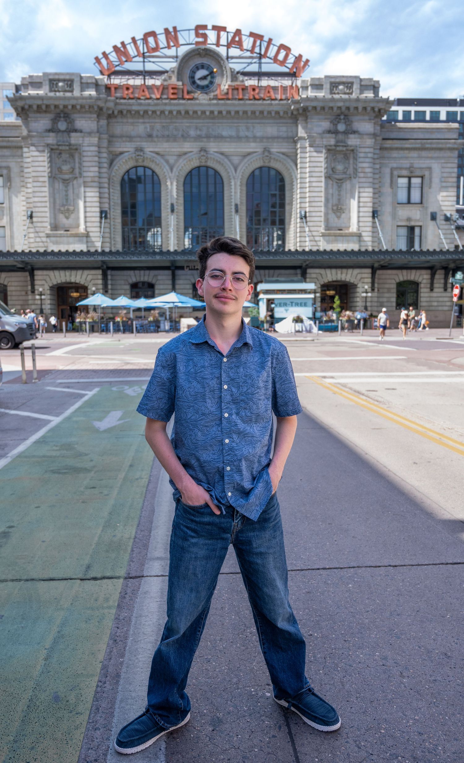 Young man in blue shirt and jeans standing in front of Denver Union Station travel hub.