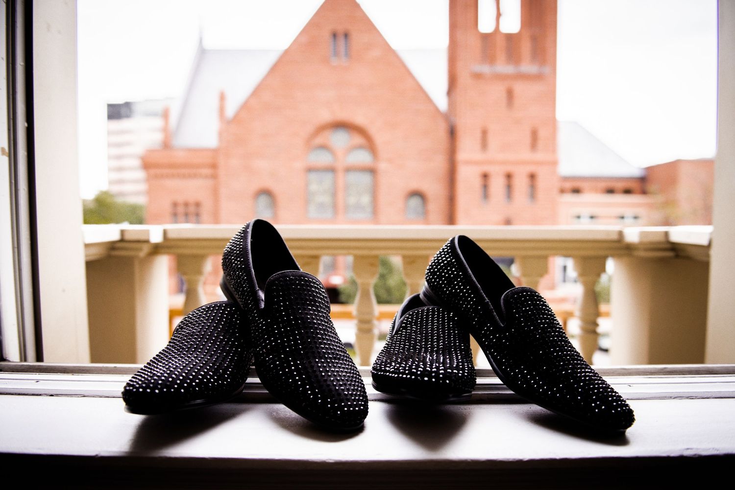 Two pairs of black rhinestone studded loafers displayed on windowsill with church in background.